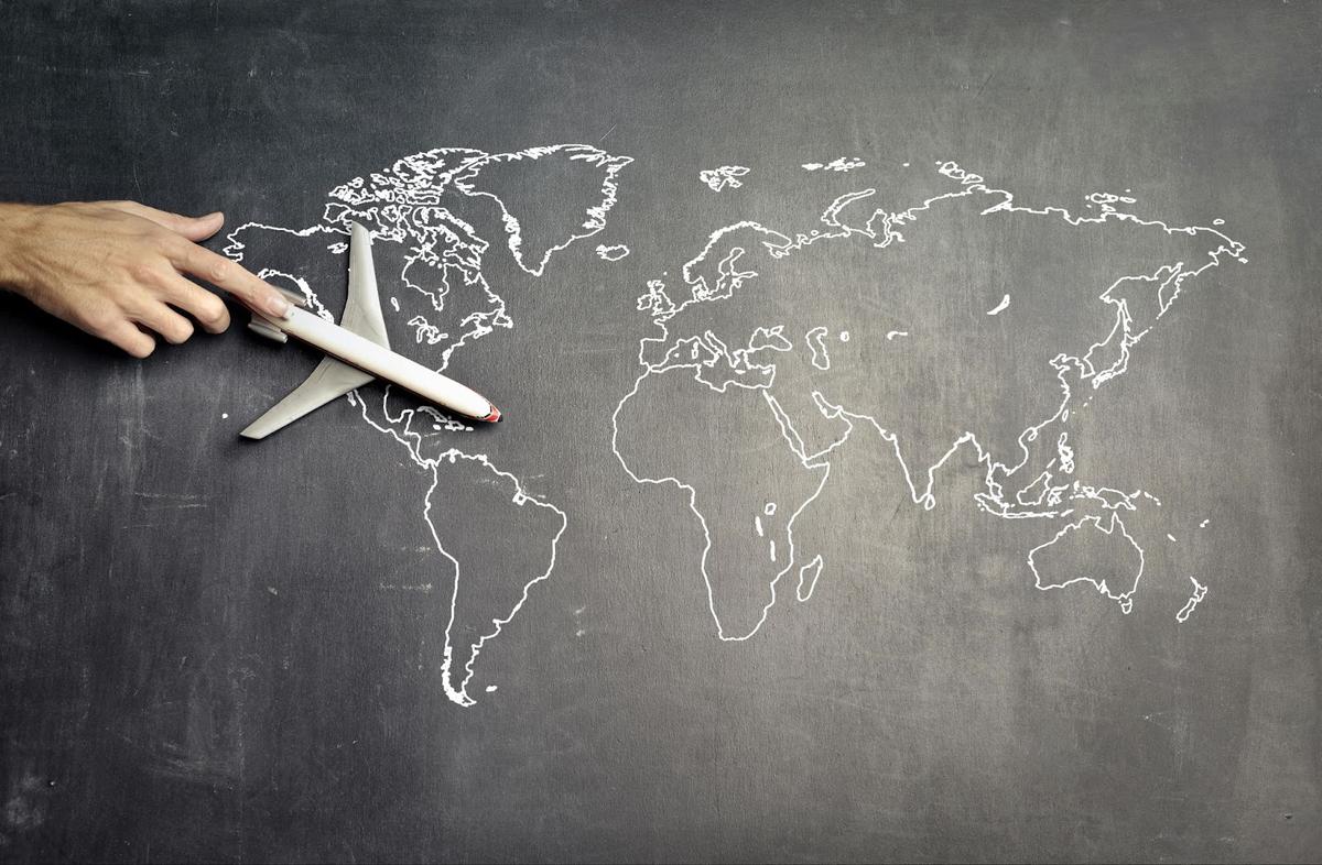 A hand guiding an airplane across a world map sketched on a chalkboard, symbolizing global aviation routes, supply chains, and the interconnected nature of spare part sourcing and pricing.