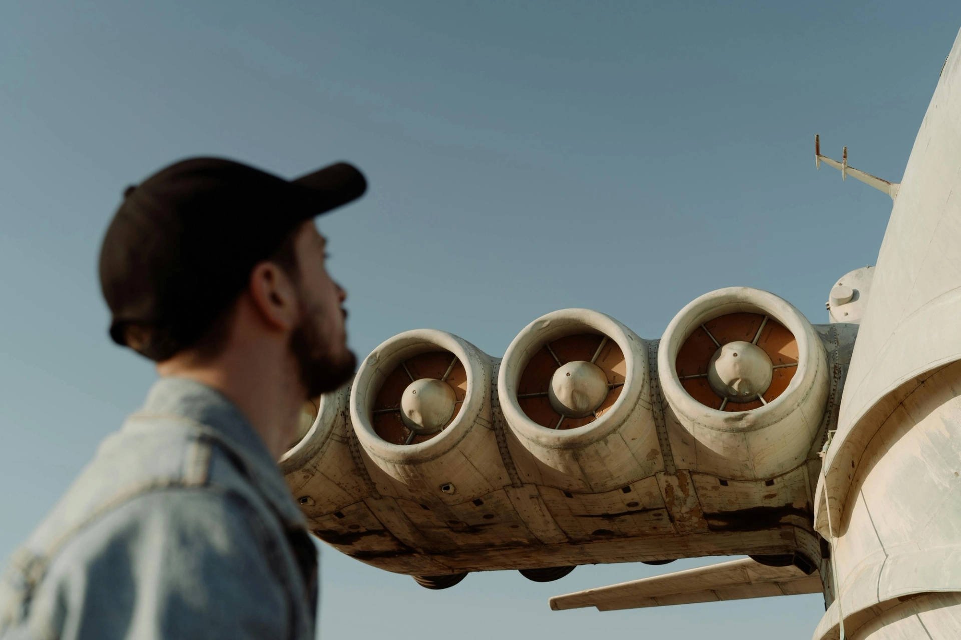 Um mecânico de jaqueta jeans e boné olha para os motores de uma aeronave antiga, mostrando o lado humano da manutenção da aviação em meio às crescentes demandas da indústria.