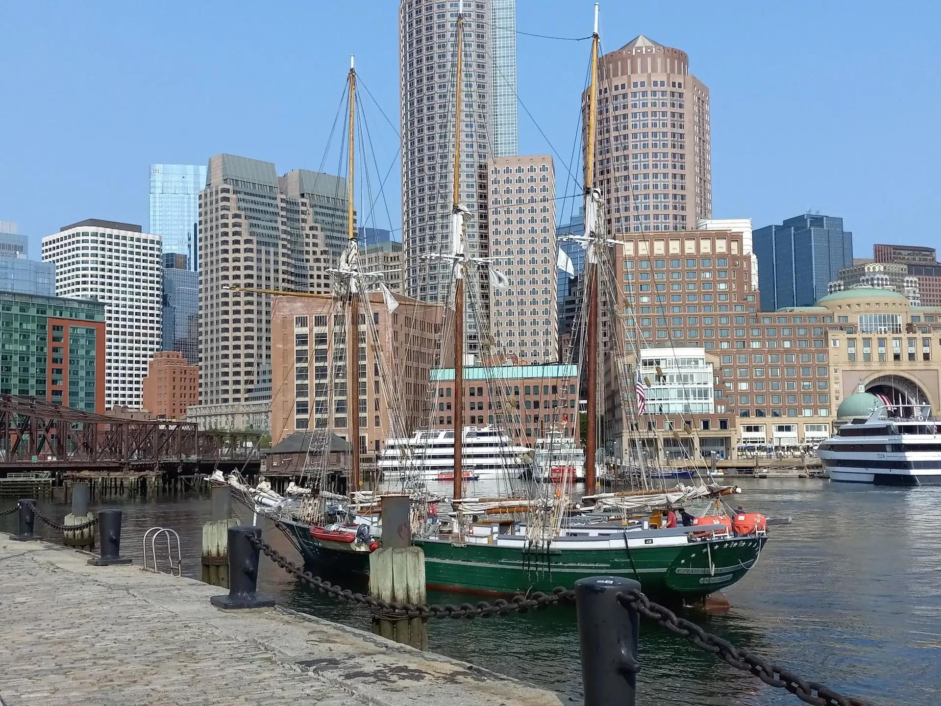 A green hulled schooner docked in front of the Boston skyline