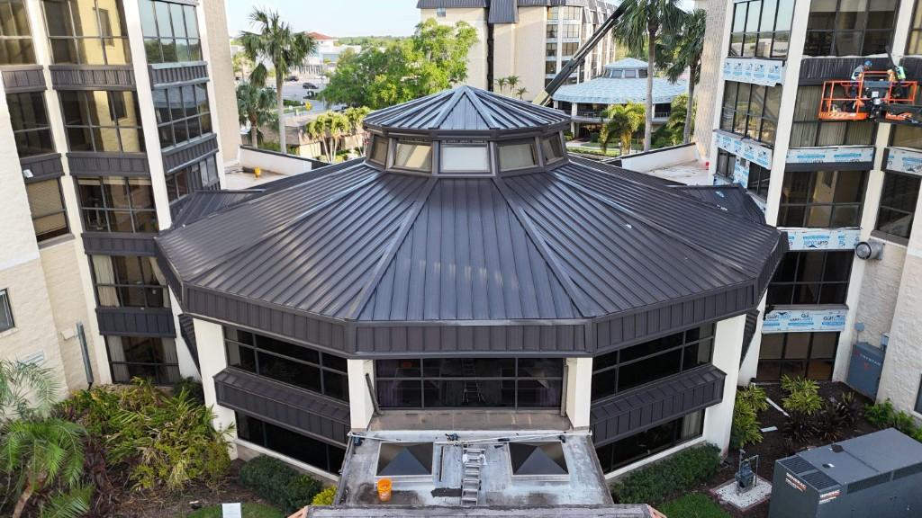Dark bronze aluminum standing-seam metal roof on an octagonal rotunda between condo towers in Seminole, seen from a drone