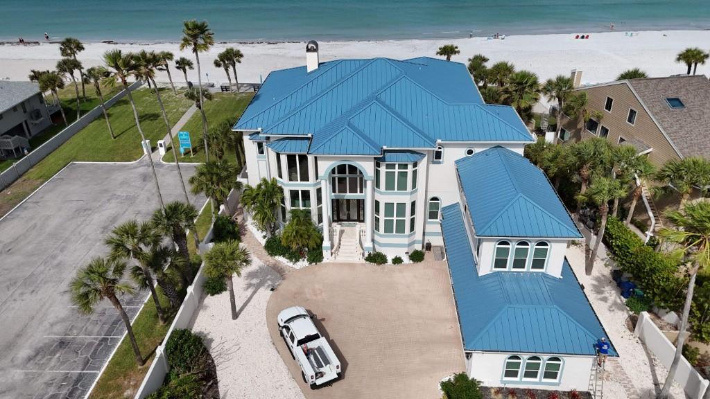 Light-blue aluminum standing-seam metal roof on a white Gulf-front home in Belleair Shores, the beach behind it, seen from a drone