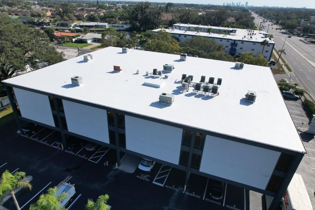 White GAF TPO flat roof with rooftop units on a three-story office building in St. Petersburg, the city skyline in the distance, seen from a drone