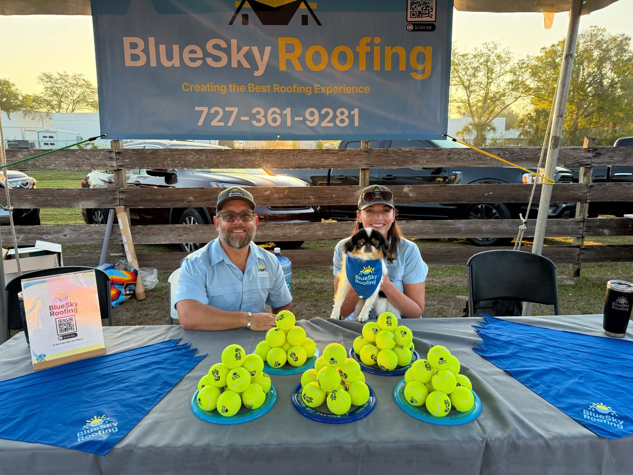 Blue Sky Roofing crew and a dog at the SPCA Tampa Bay Pet Walk booth, with tennis balls stacked on the table