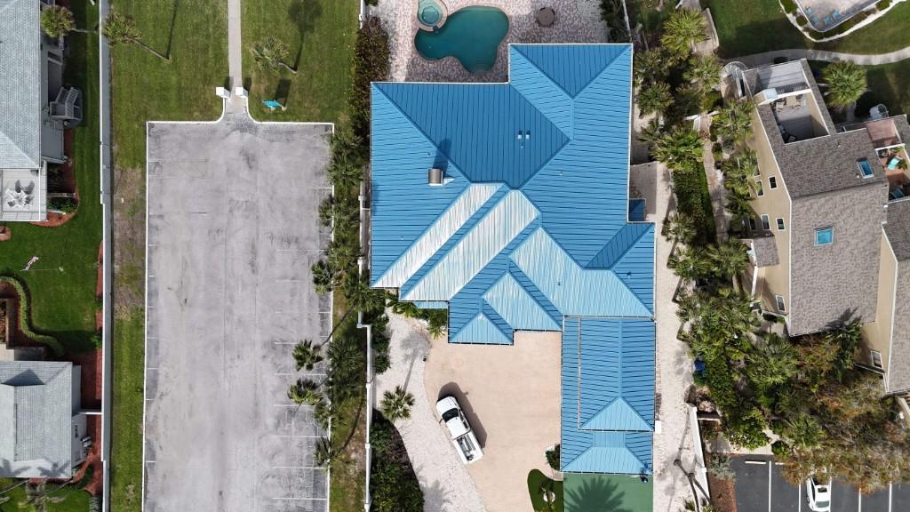 Light-blue aluminum standing-seam metal roof on a Gulf-front home in Belleair Shores, seen straight down from a drone beside the pool and driveway