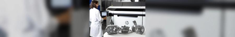 A technician in a lab coat operates the touchscreen of an HP Multi Jet Fusion 3D printer, with several finished additive-manufactured parts displayed on the table in front of the machine.