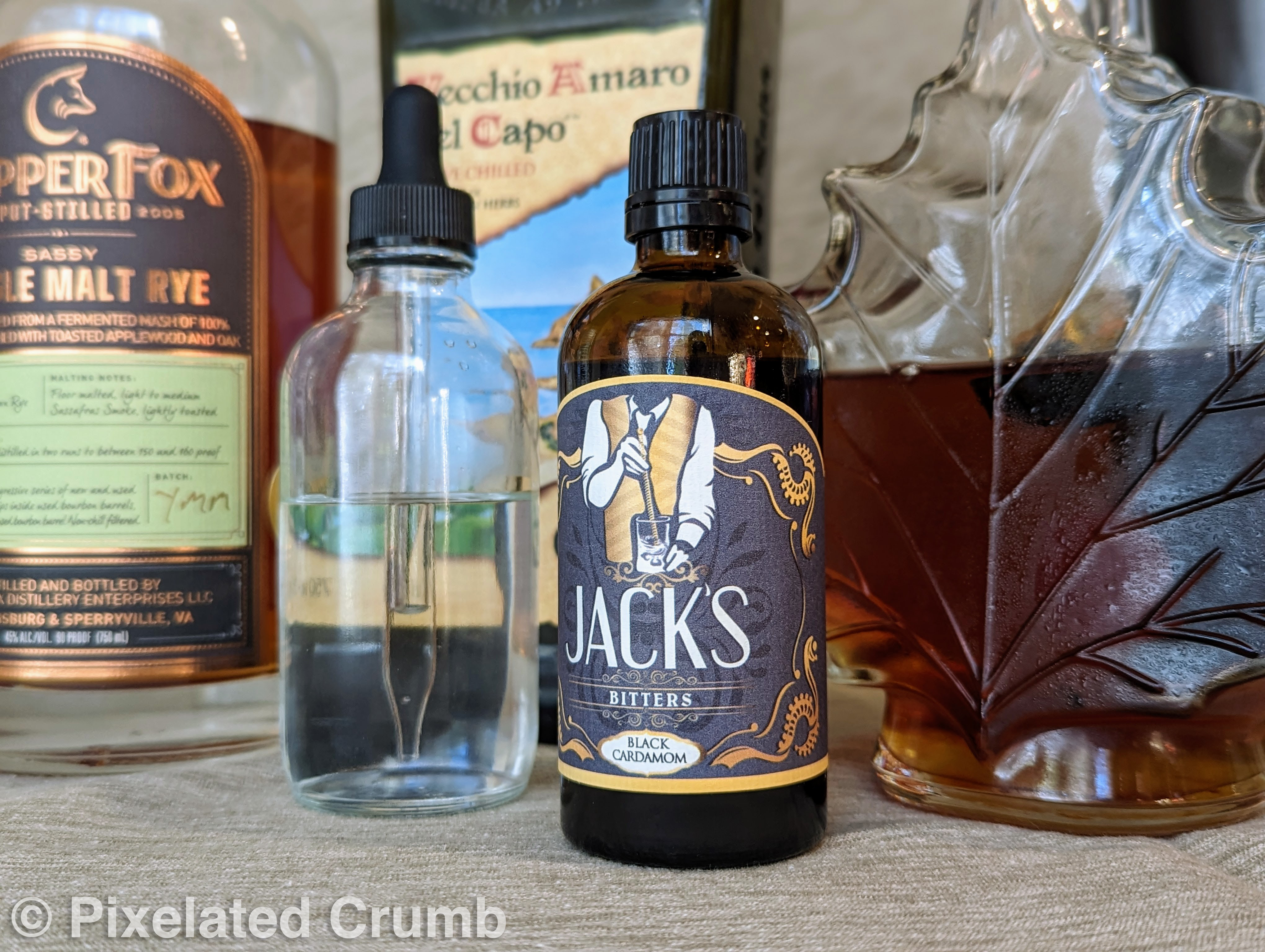 Bottles of jack's black cardamom bitters, salt water, maple syrup, rye, and amaro 