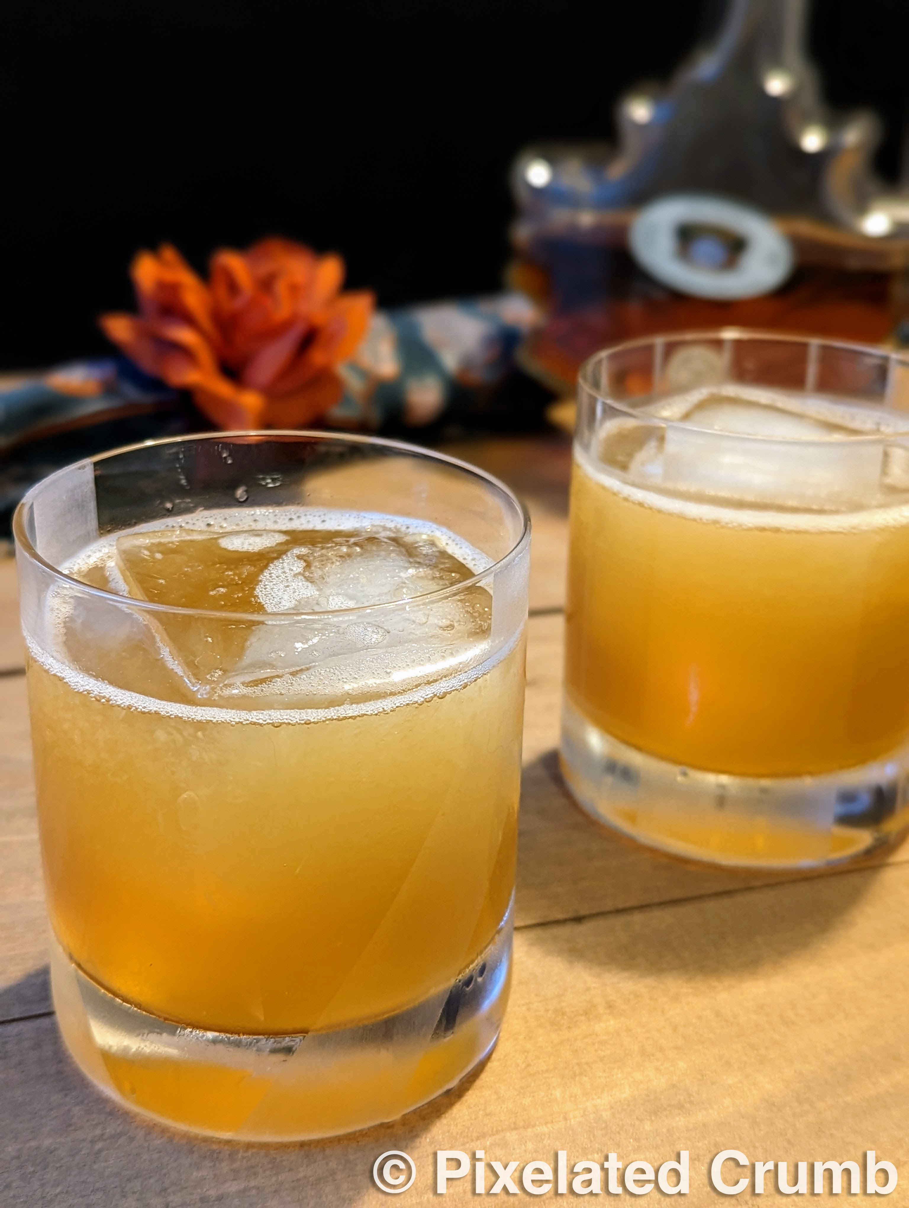 Two rocks glasses with deep golden cocktails over large squares of ice