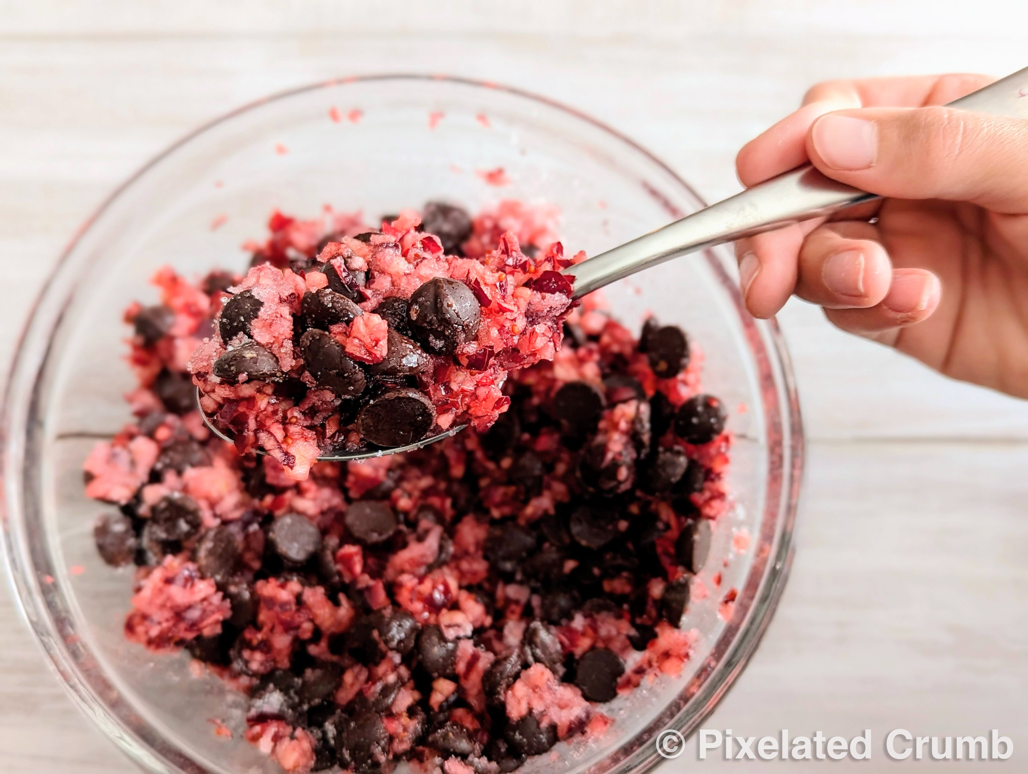 A child's hand mixing cranberries, chocolate chips, sugar, and cinnamon. 