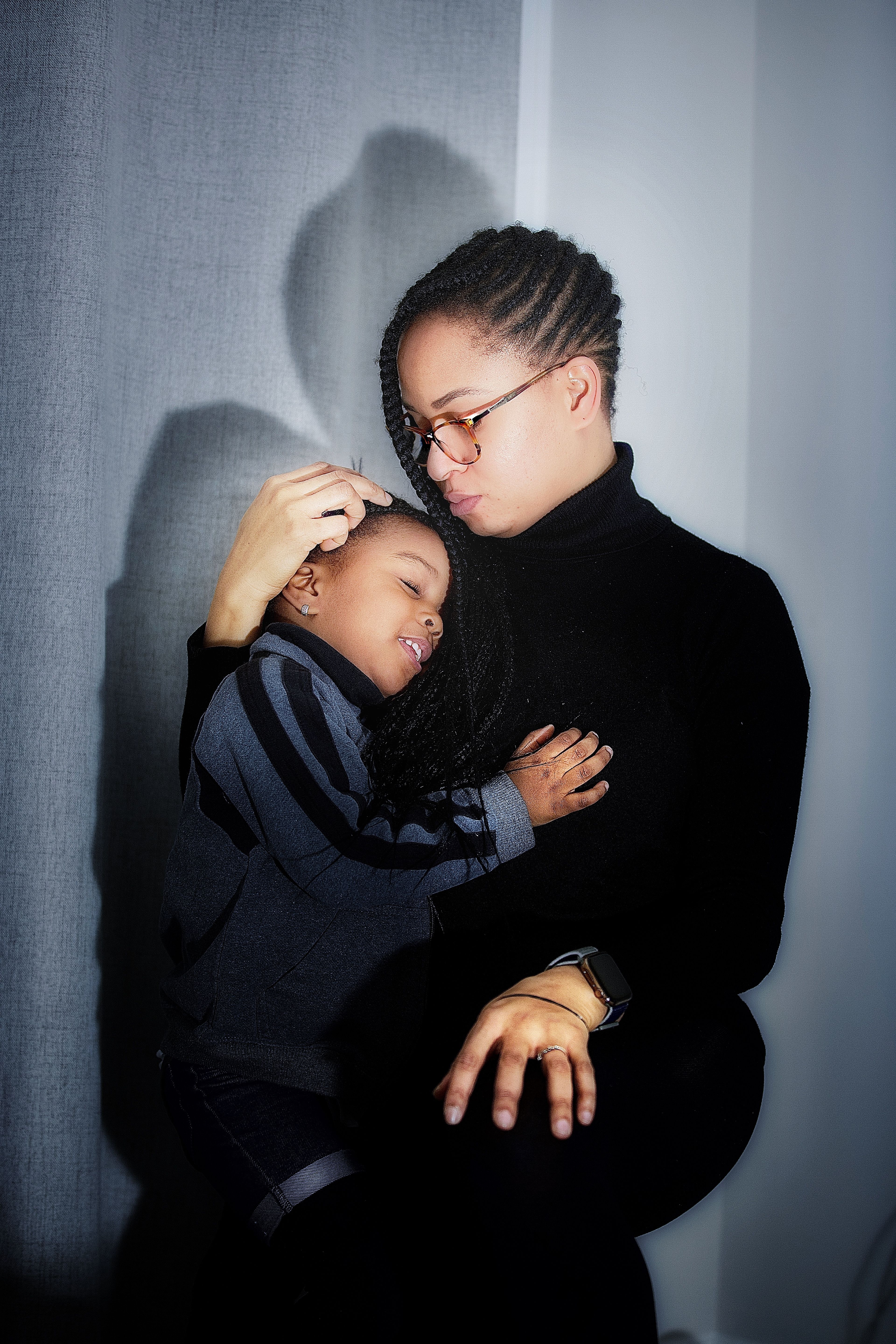 Mother holding her son close against a soft grey wall
