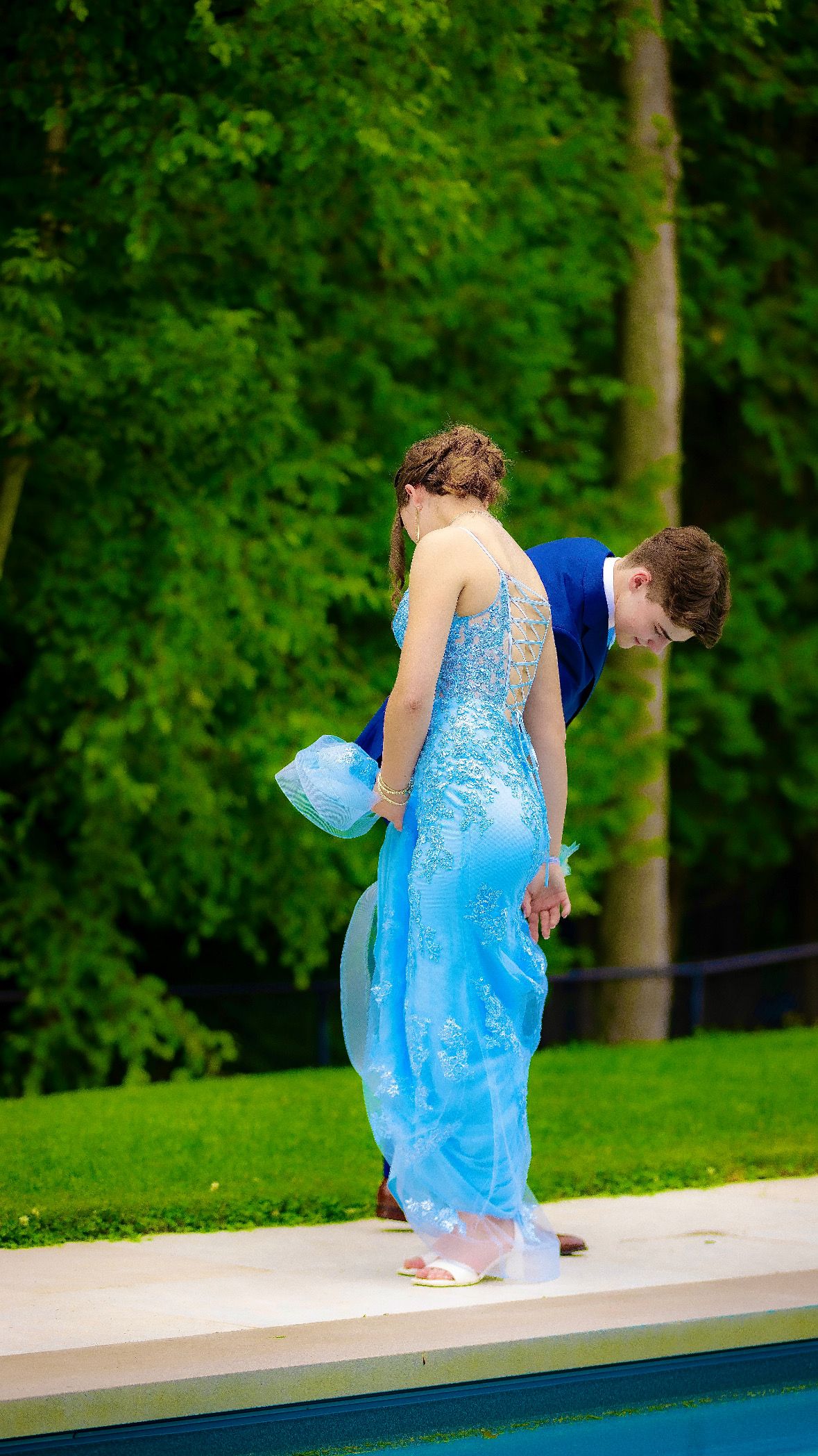 Couple gathering the length of a gown beside a pool