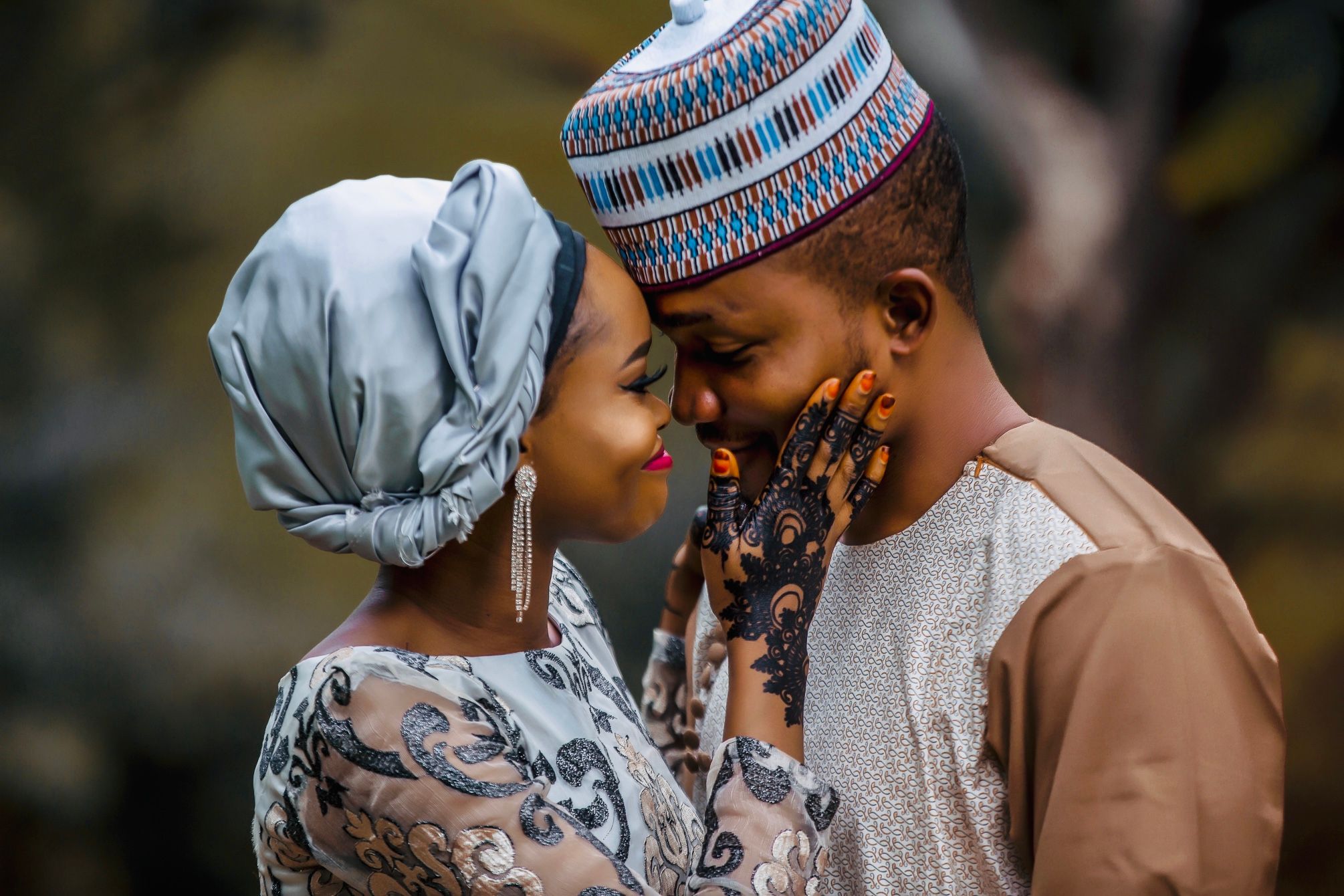 Bride and groom forehead to forehead, her henna-painted hand resting on his cheek