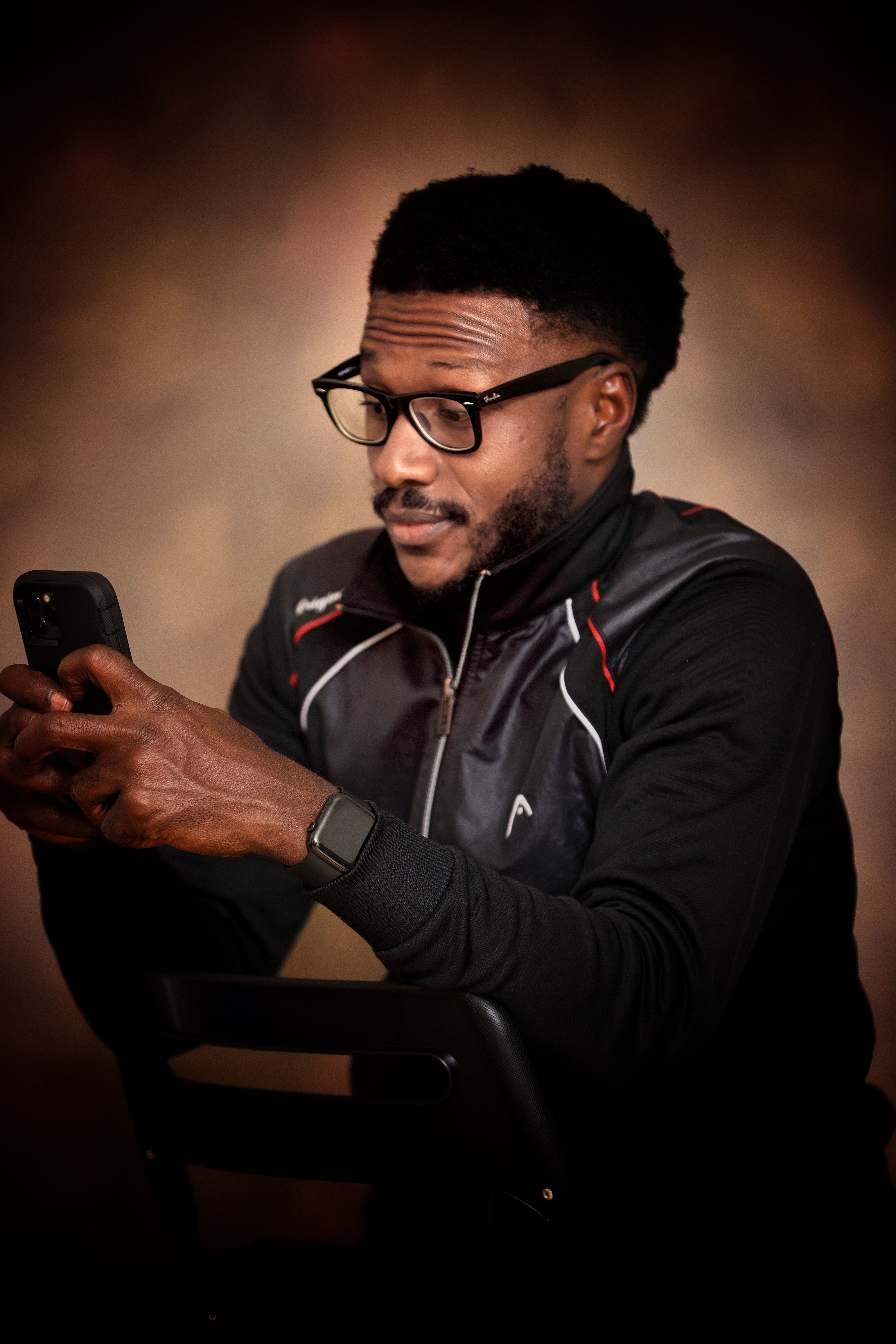 Man in glasses and a track jacket looking down at his phone in the studio