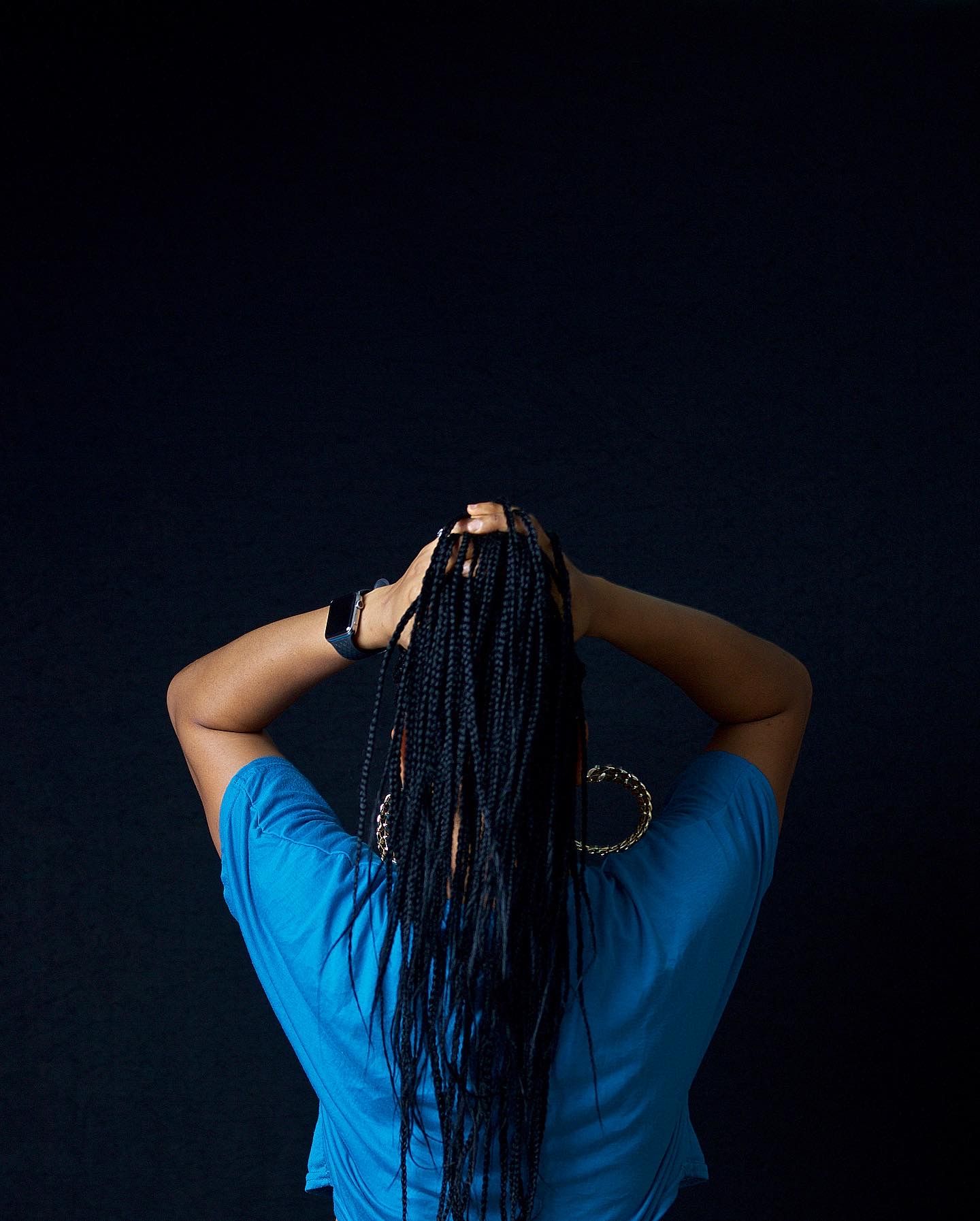 Dramatic portrait from behind with long braids against a dark background