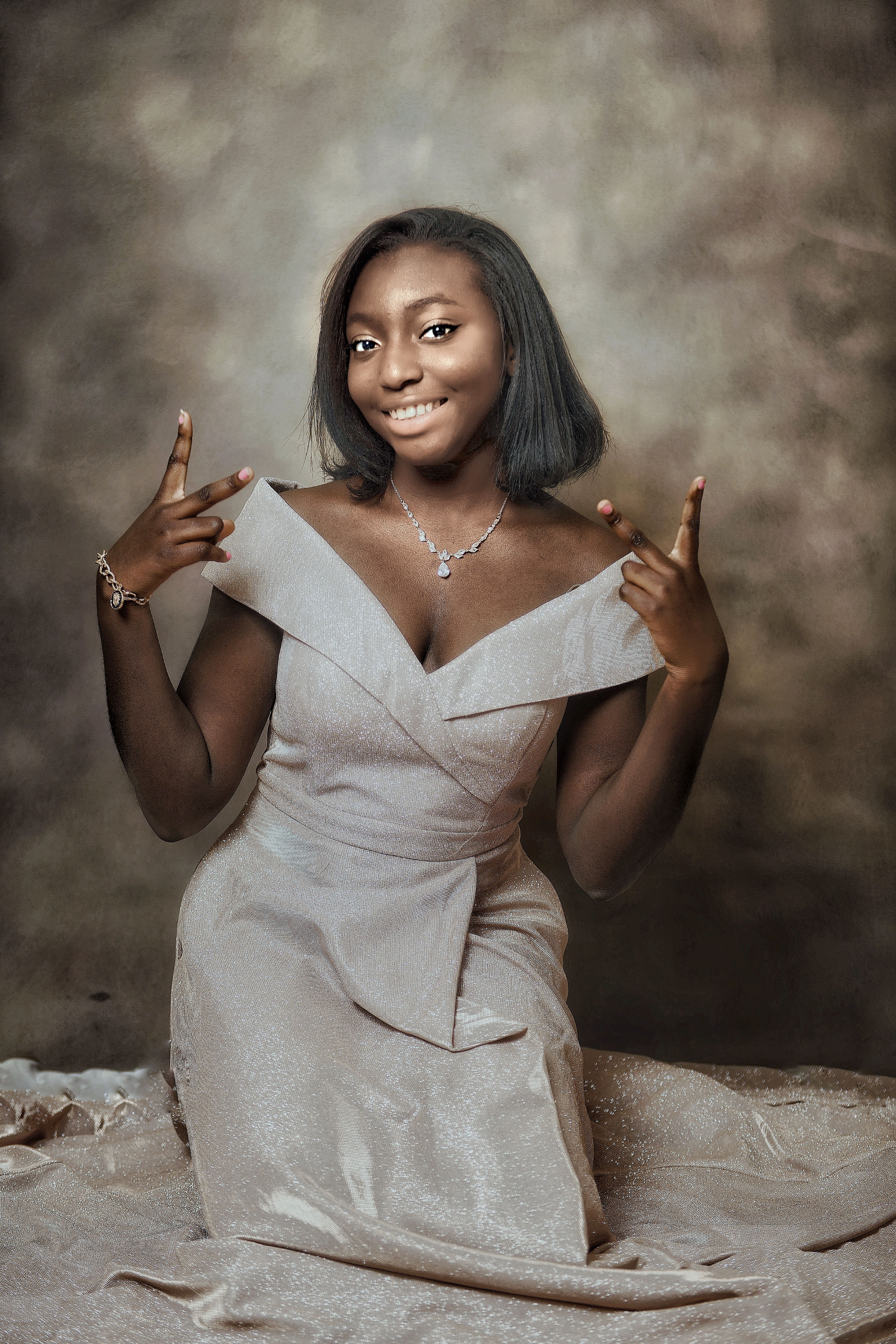 Studio portrait in a champagne off-shoulder gown, hands raised in a playful pose