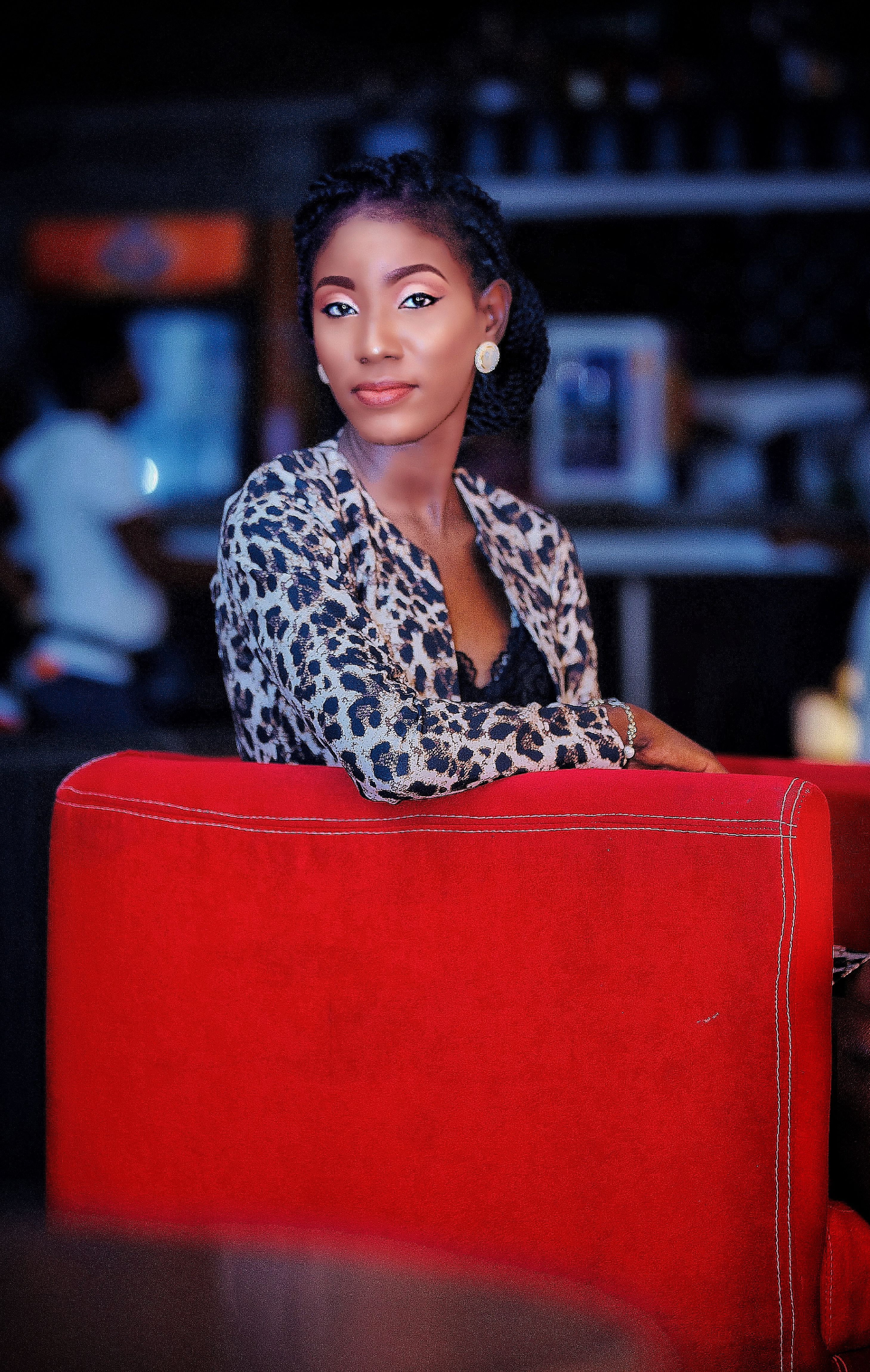Woman in a leopard-print jacket leaning on a red couch in a dim lounge