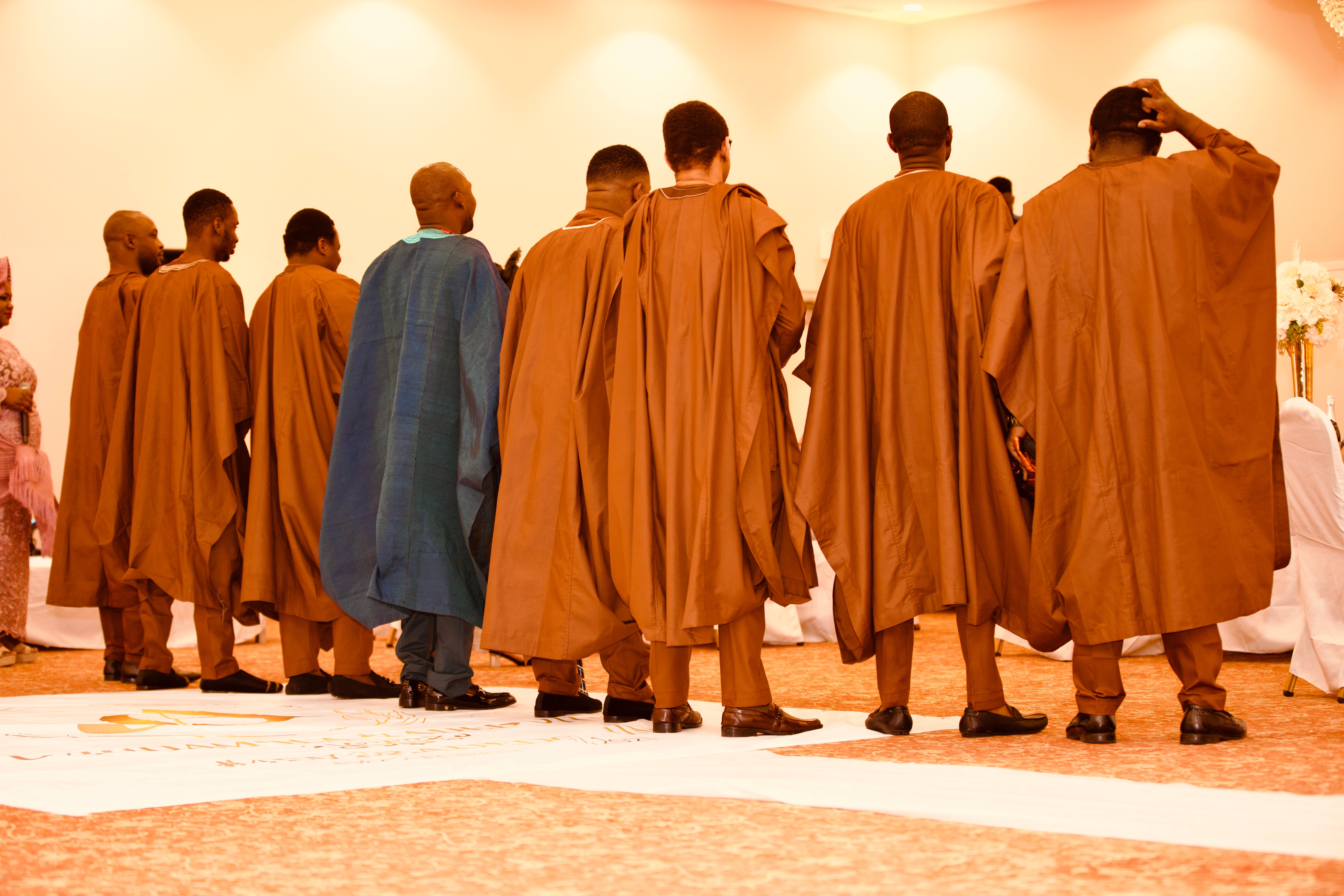 Row of men in matching brown agbada robes seen from behind at the ceremony