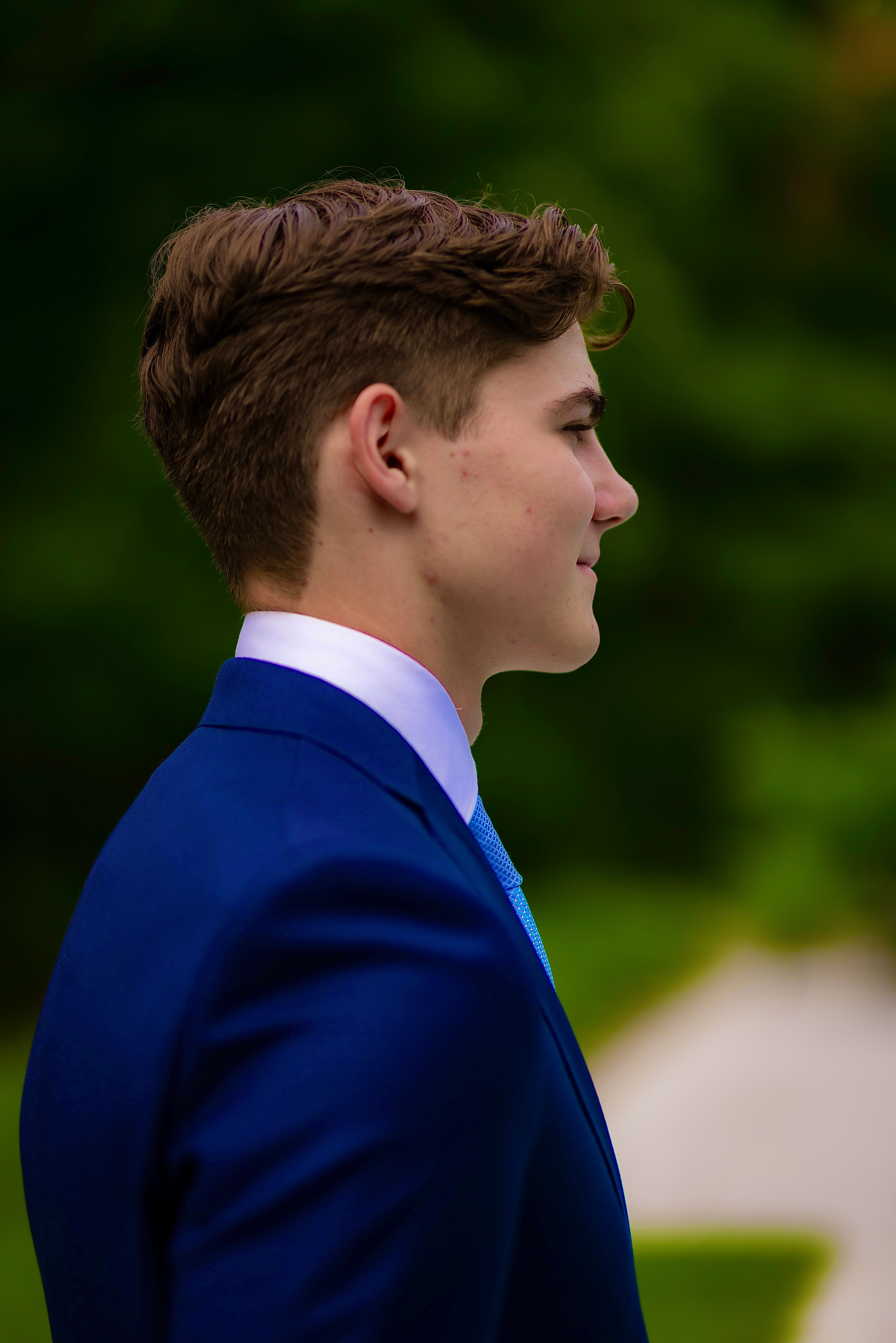 Graduate in a navy suit and blue tie, profile against summer greenery