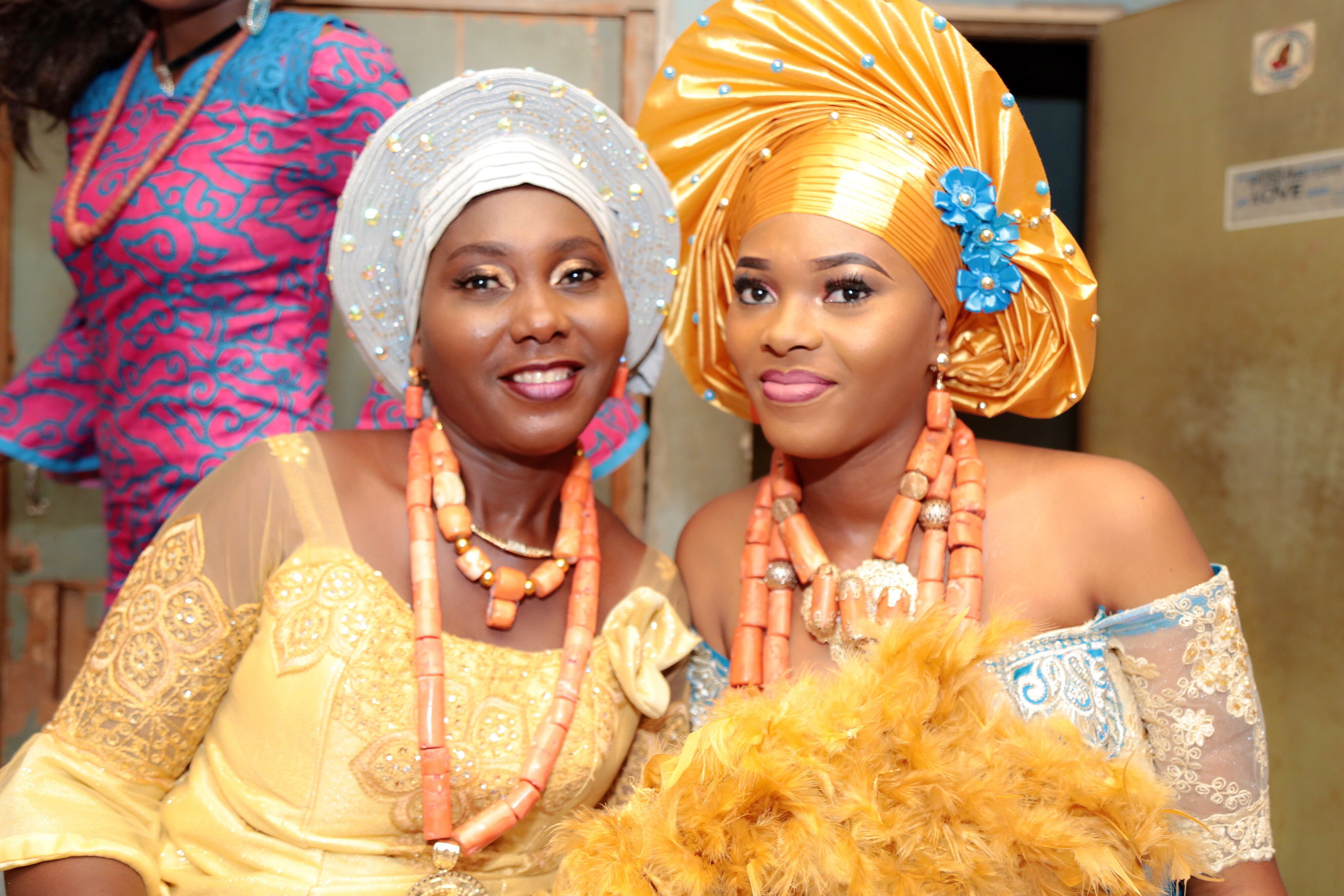 Two women in gele headwraps and coral bead necklaces before the ceremony