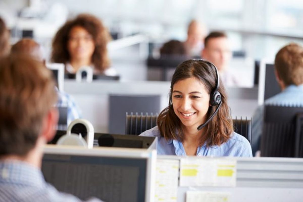 female customer service representative in a call center smiling while surrounded by her coworkers