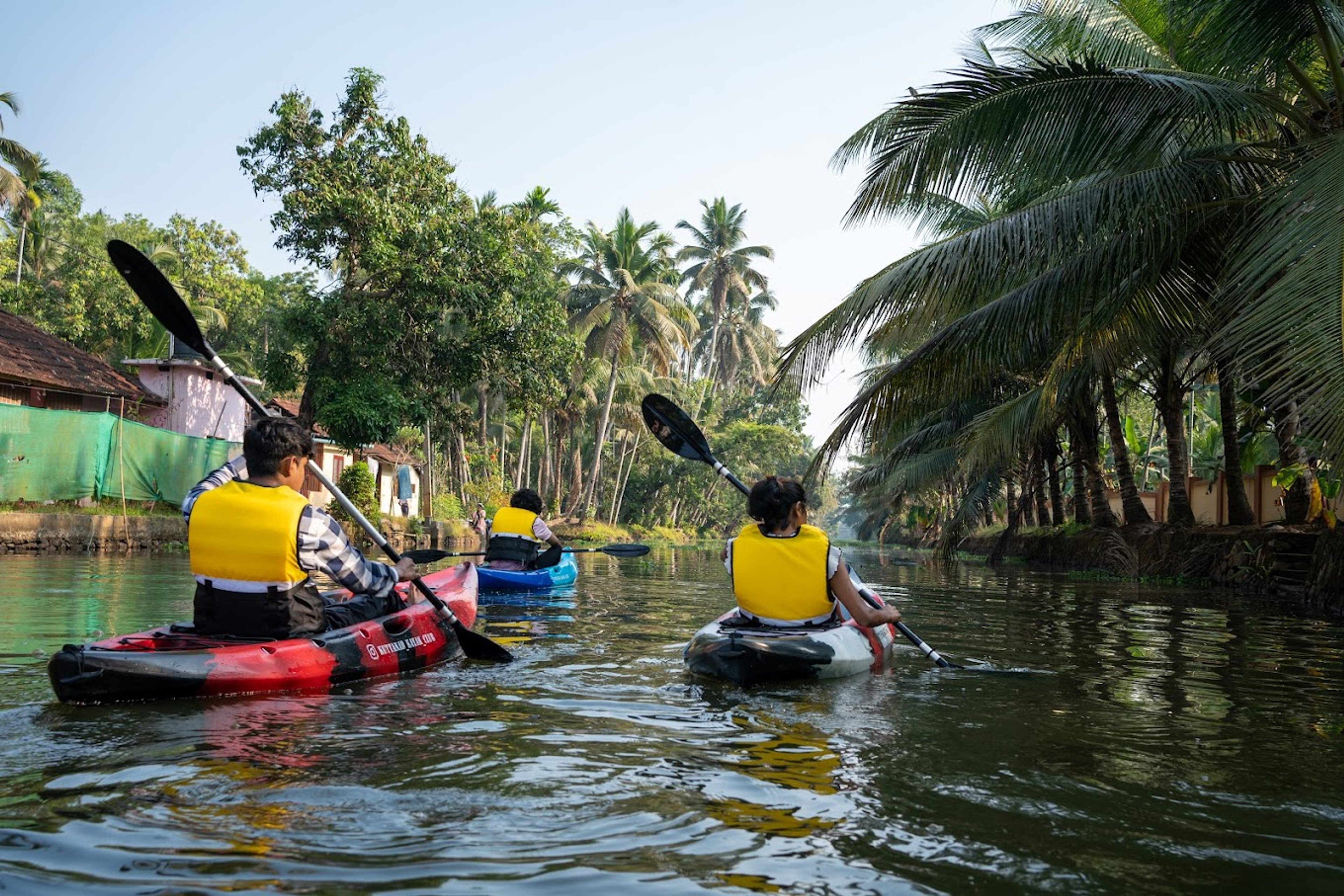 Guests in life jackets kayaking down a palm-lined canal in Alleppey