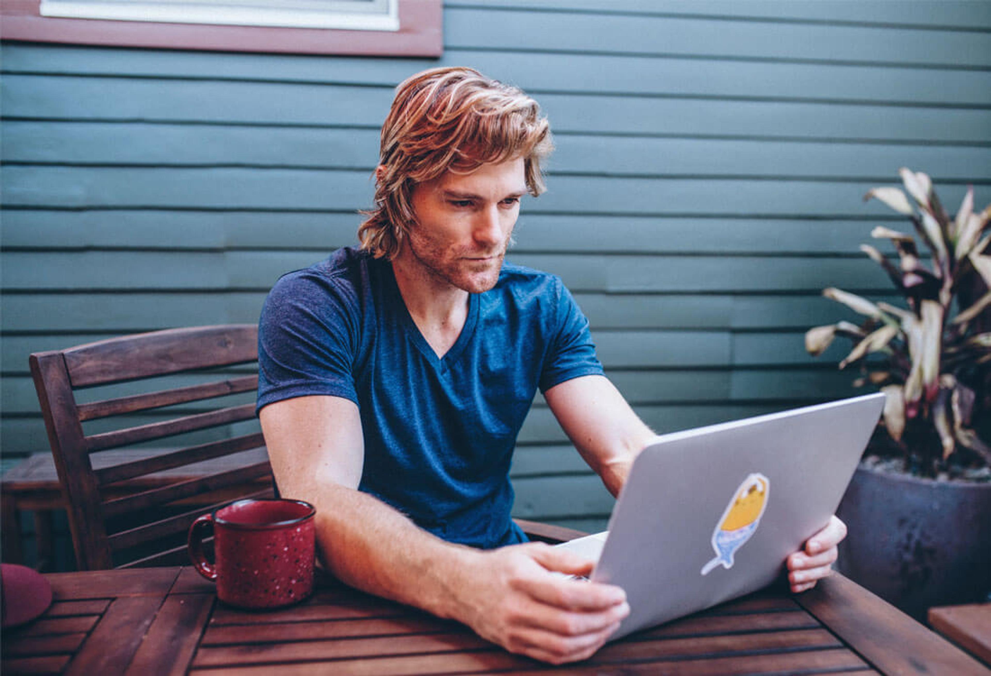 Persoon met t-shirt die op zijn laptop zit