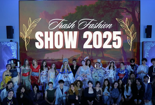 Trash Fashion Show participants pose in front of a screen with the words "Trash Fashion Show 2025" displayed.