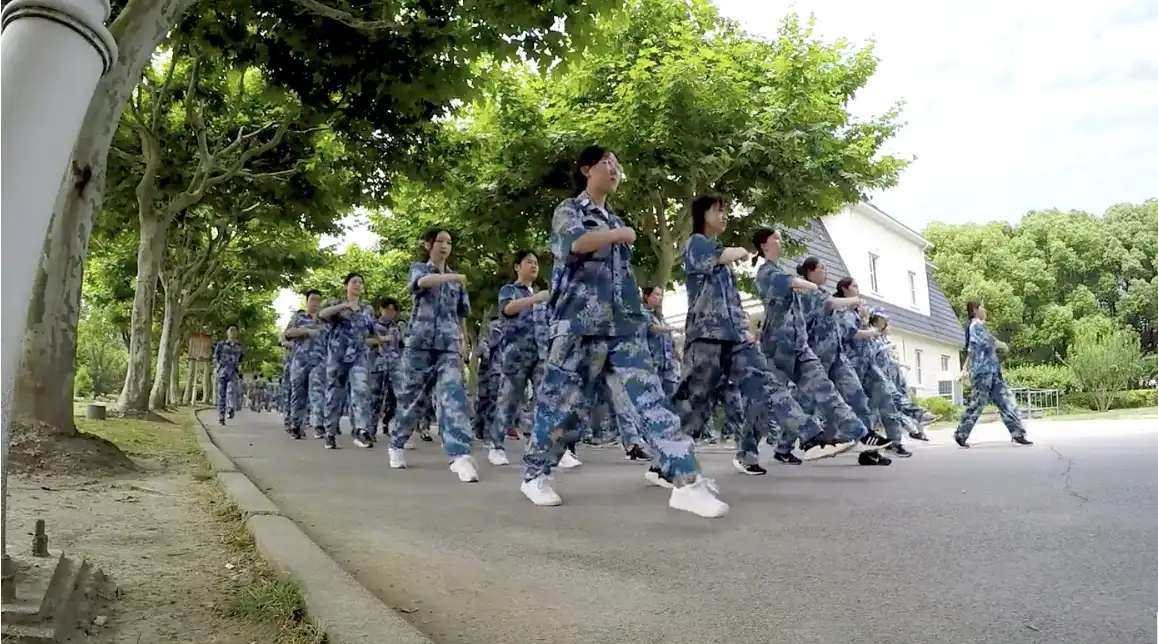 An array of students dressed in blue military uniforms marching in lockstep down a street