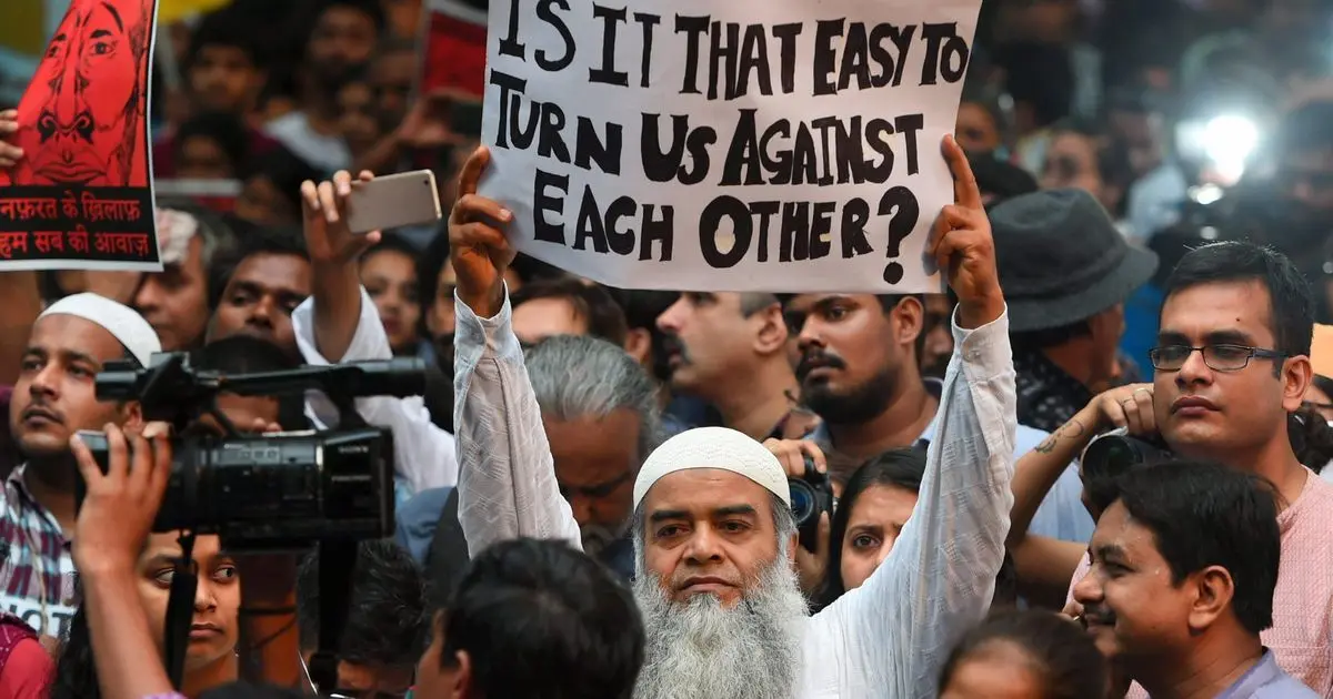 A protestor raising a sign saying 'Is it that easy to turn us against each other?'