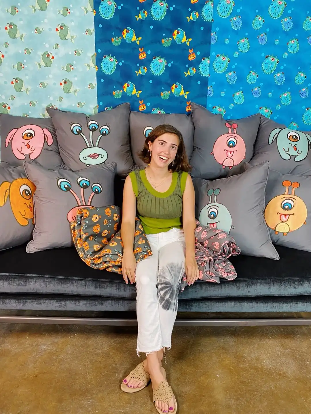 A woman sits on a couch surrounded by pillows