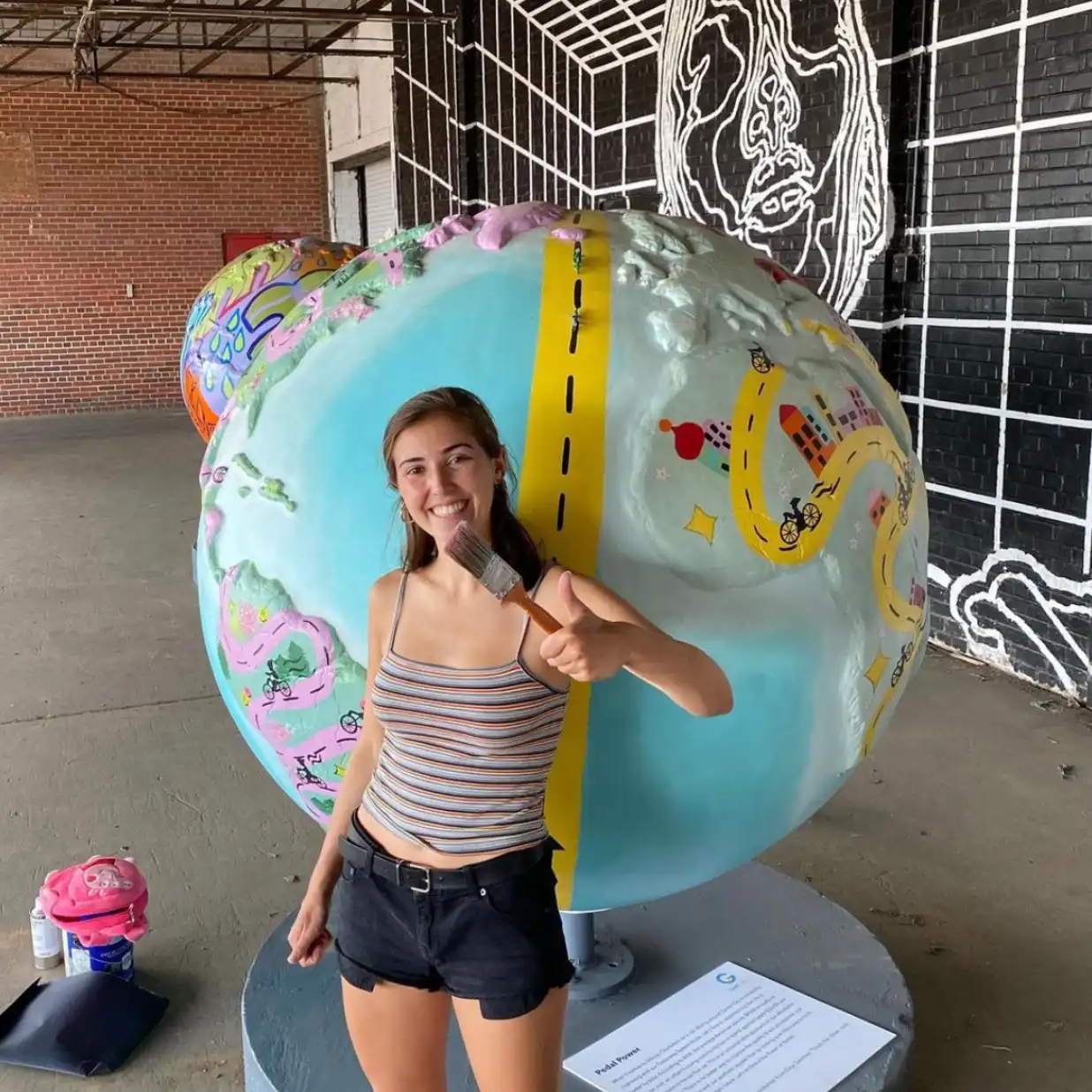 A woman holding a paint brush standing in front of a human-sized globe