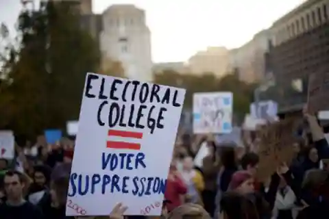 A protest and a sign stating 'Electoral College = Voter Suppression'