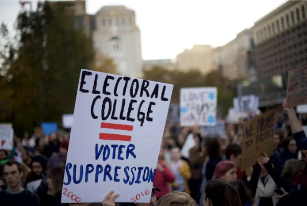 A protest and a sign stating 'Electoral College = Voter Suppression'