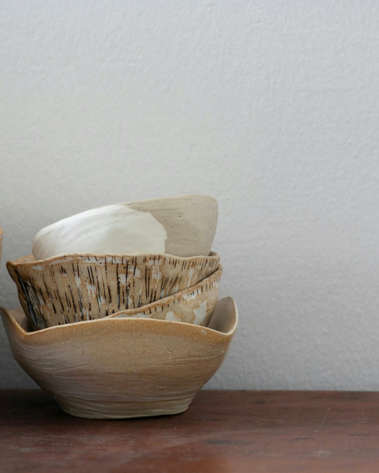A cluster of hand-thrown bowls in oatmeal and ash glazes gathered on a shelf