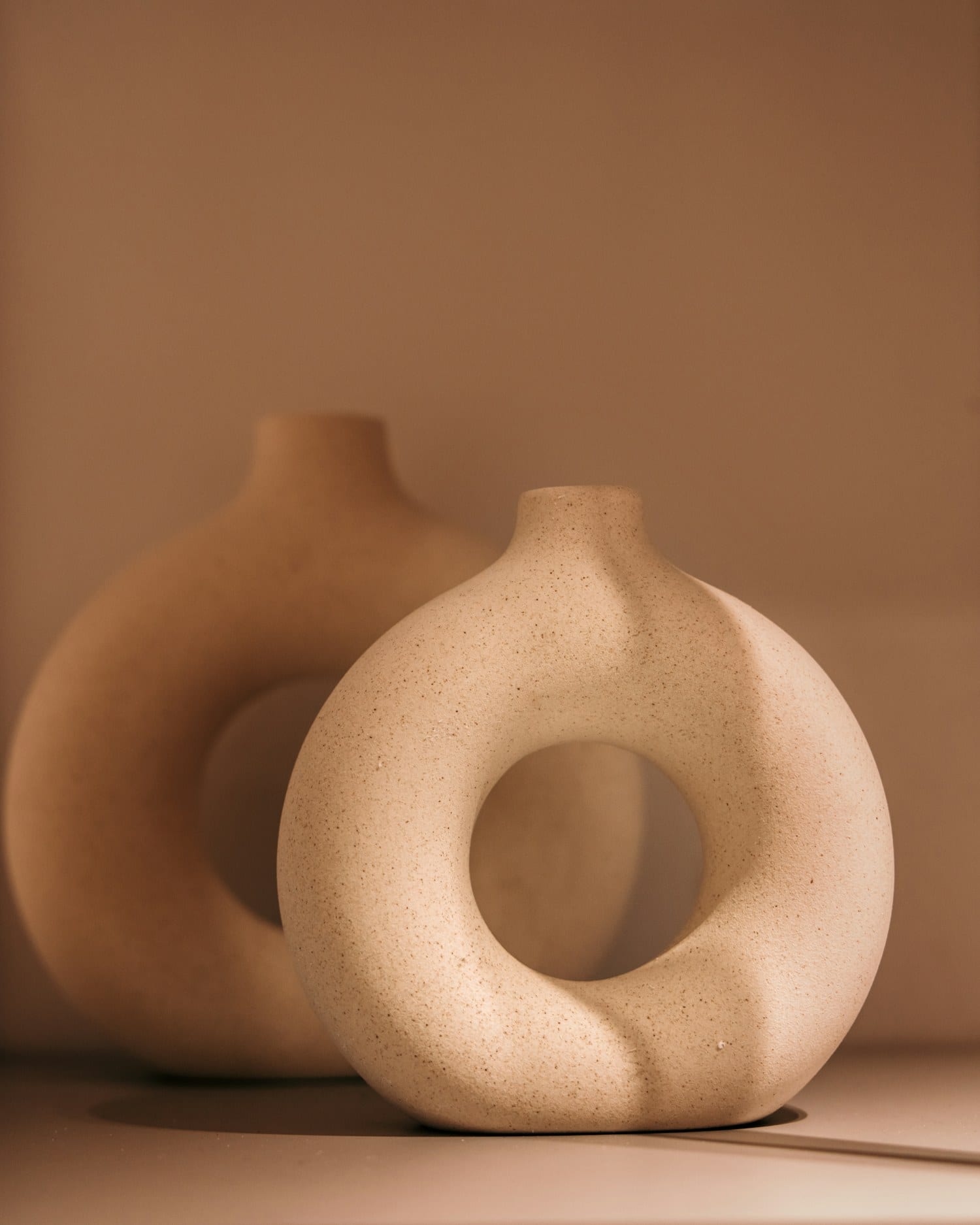 Two rounded terracotta vases of different heights against a warm ground