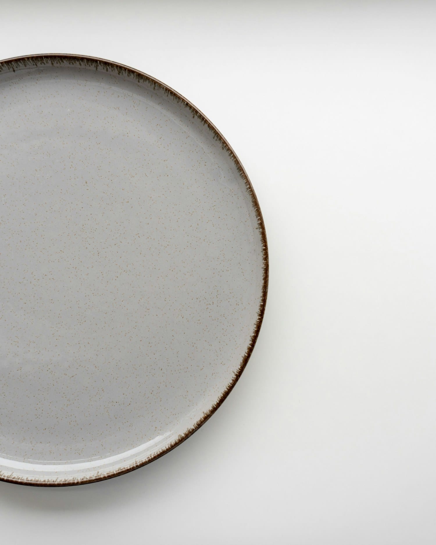 Stoneware dinner plate with an unglazed chestnut rim on a pale ground
