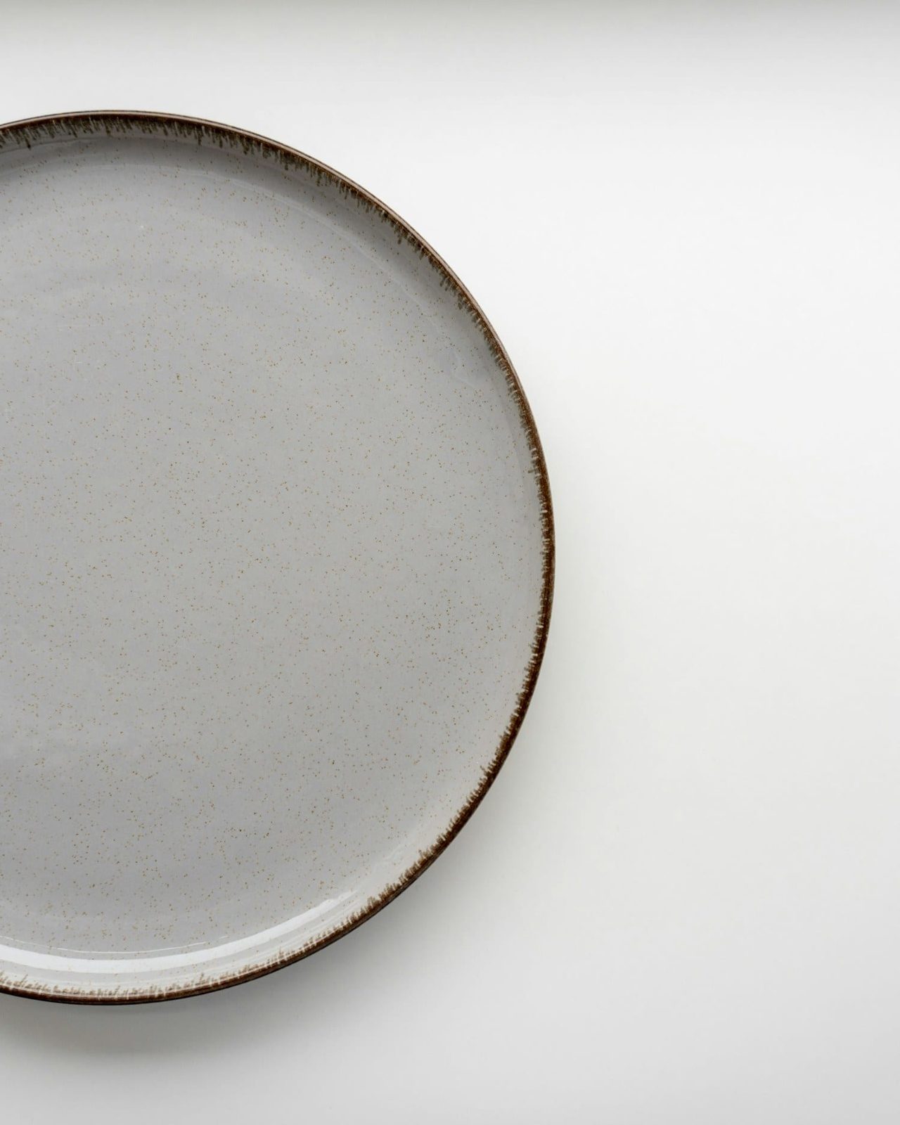 Stoneware dinner plate with an unglazed chestnut rim on a pale ground