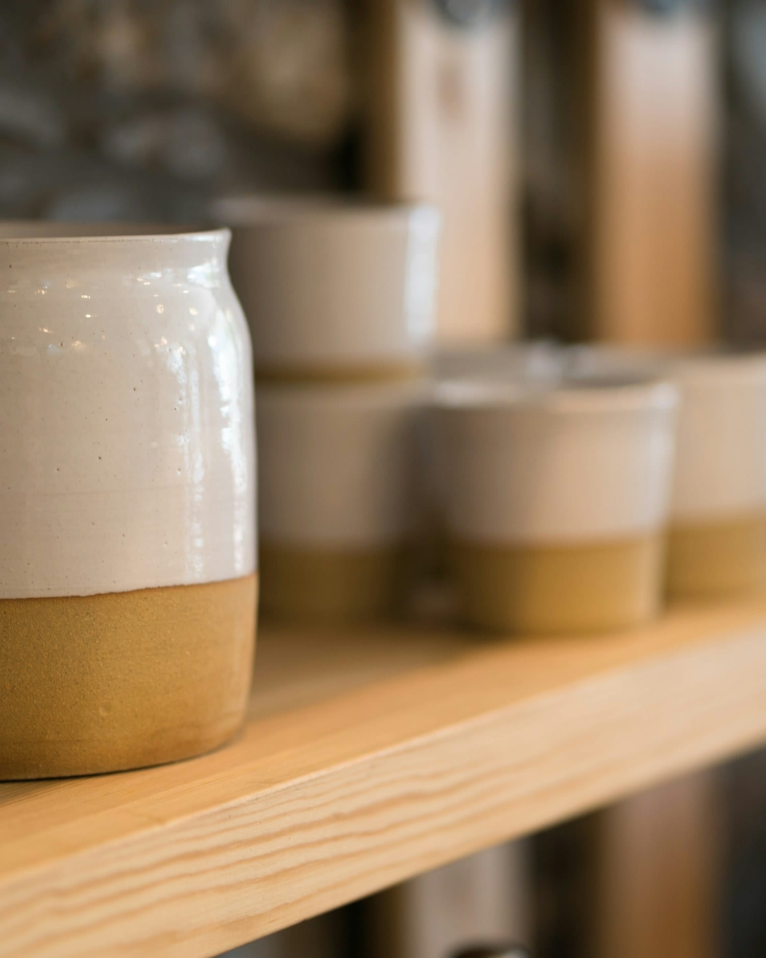 Two-tone stoneware beakers, glazed white above and left raw clay below, on a timber shelf