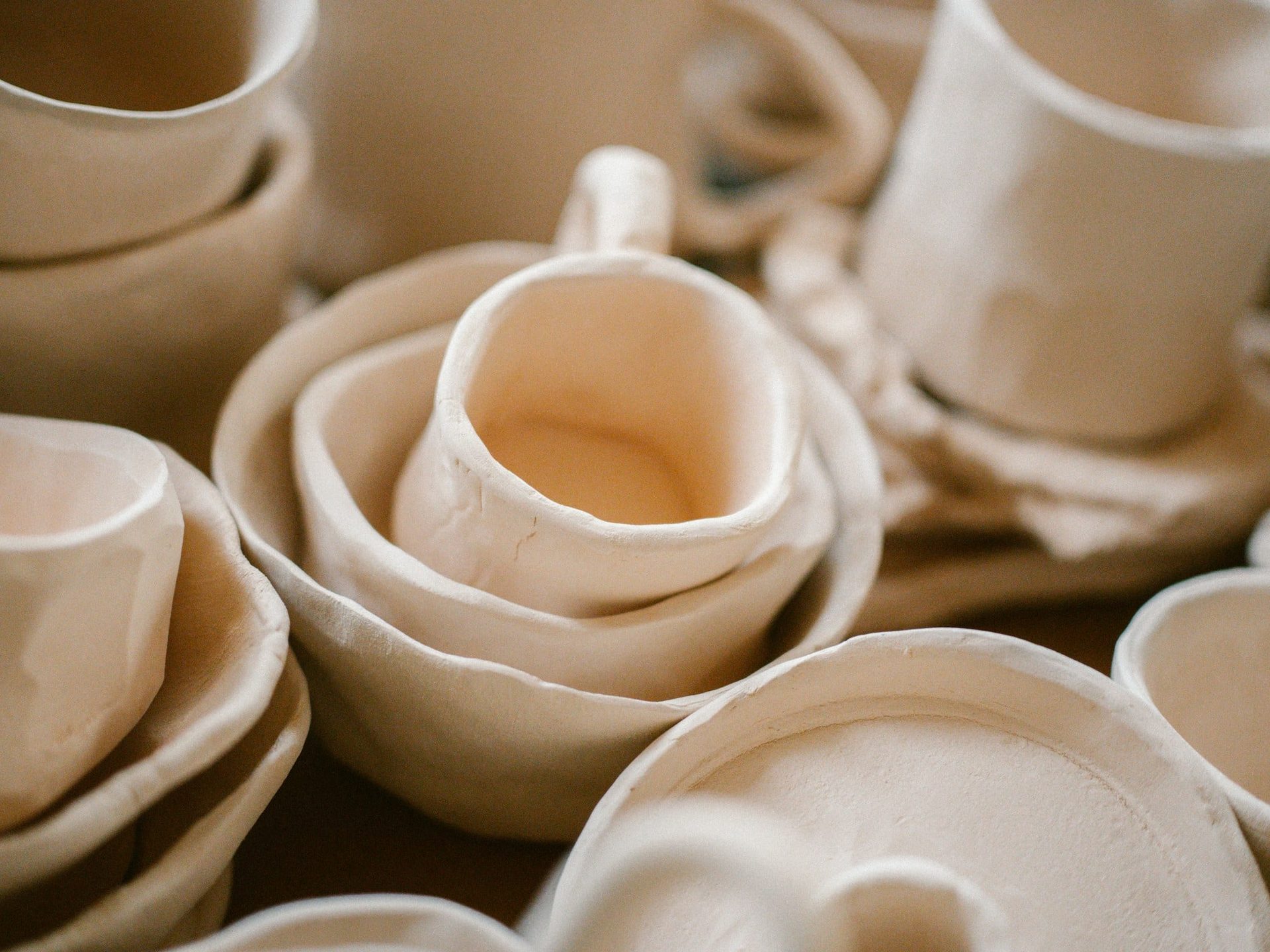 A gathered pile of cream bisque bowls, cups and jugs awaiting glaze