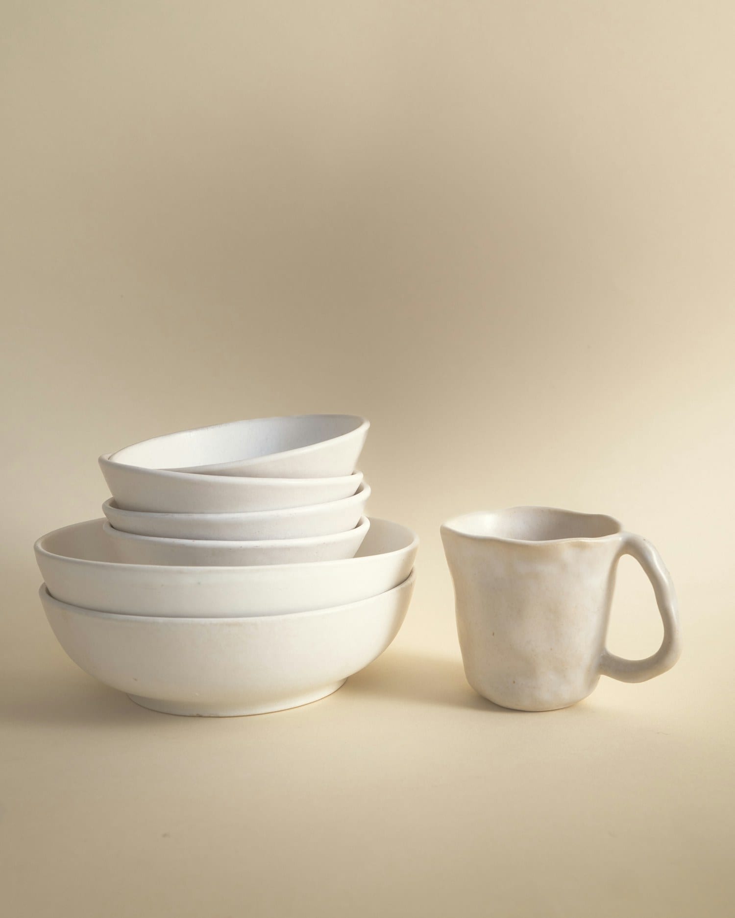 Porcelain serving bowls beside a hand-pinched pouring jug