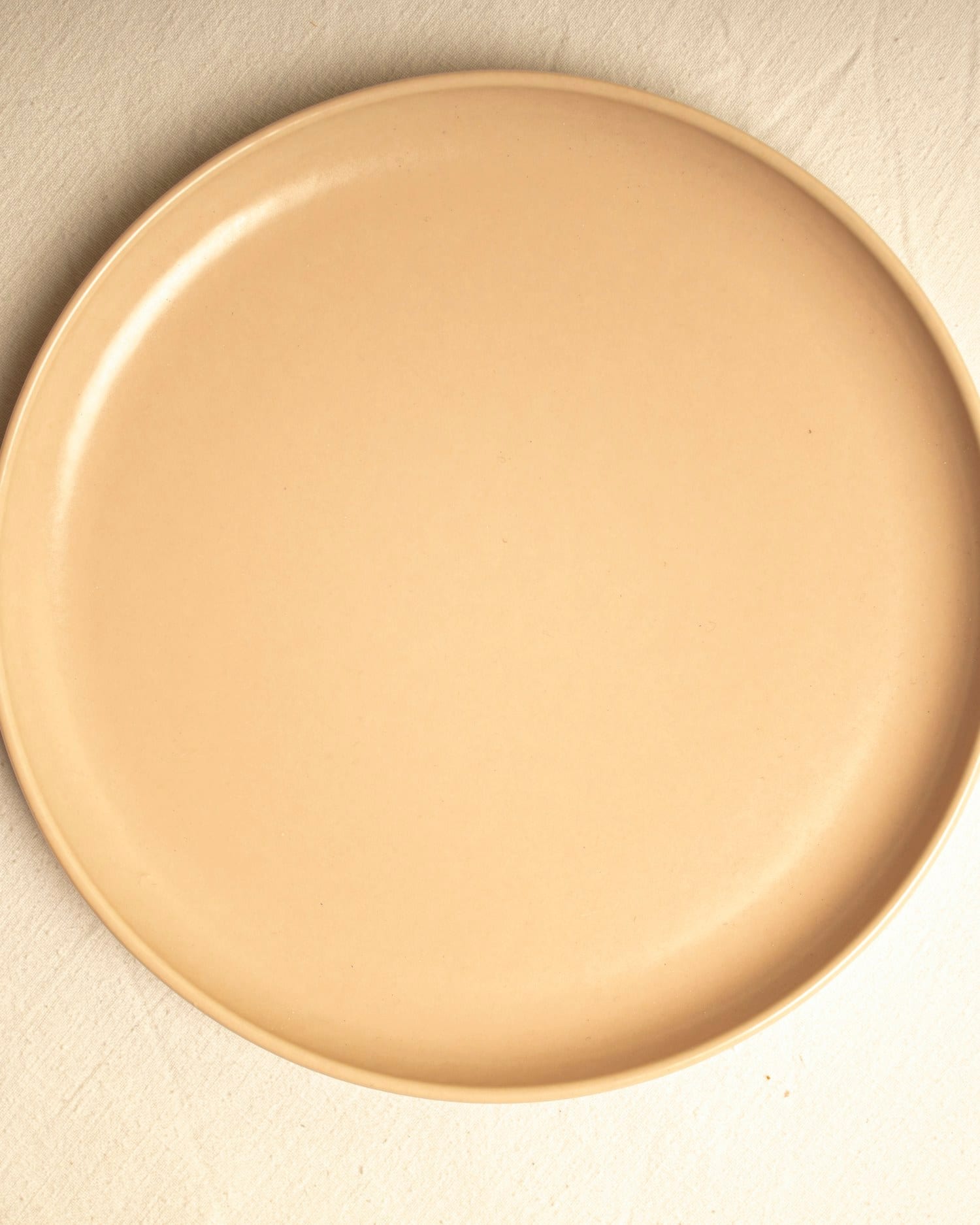 A butter-toned side plate photographed from above on a soft cream surface