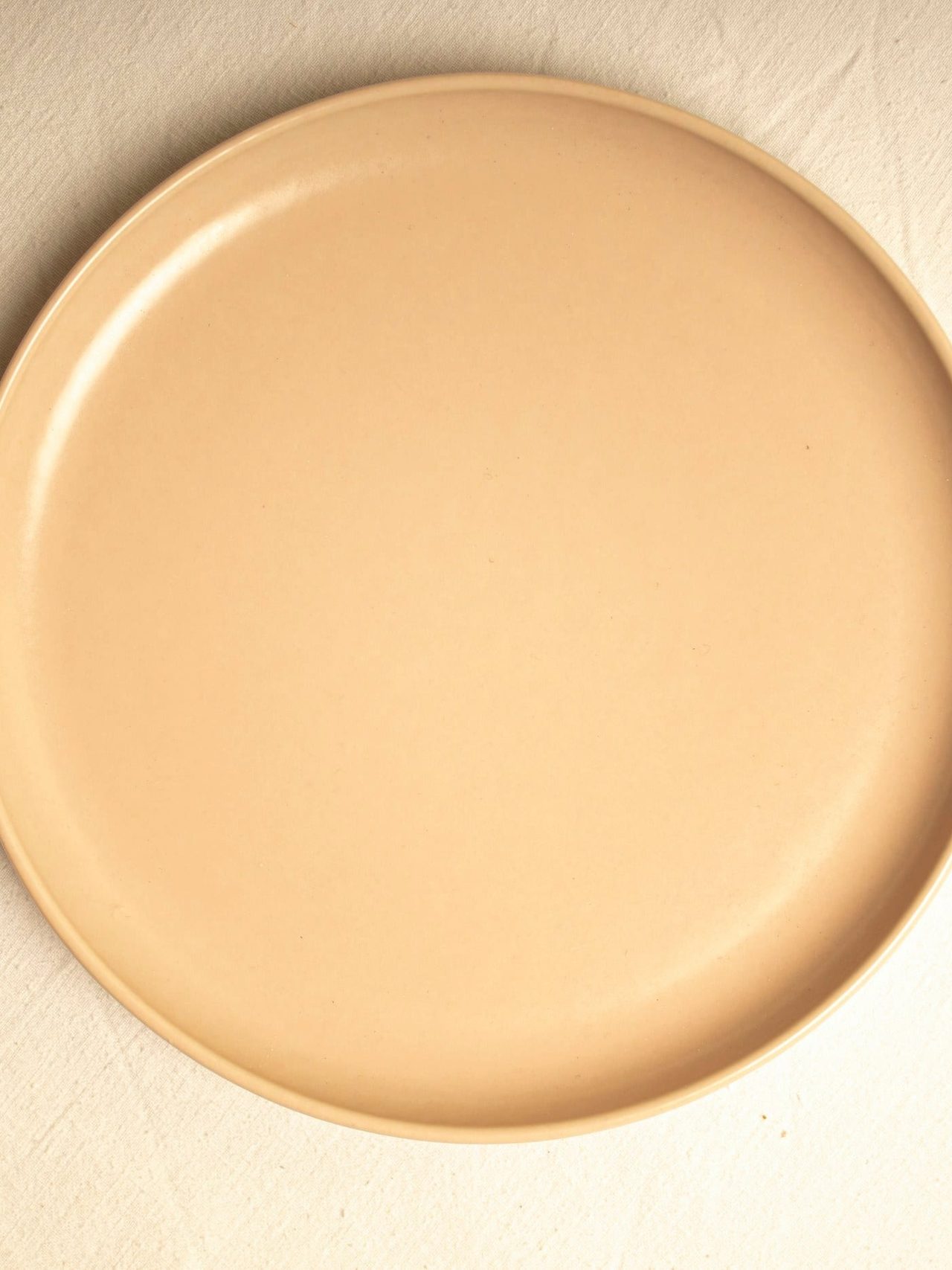 A butter-toned side plate photographed from above on a soft cream surface