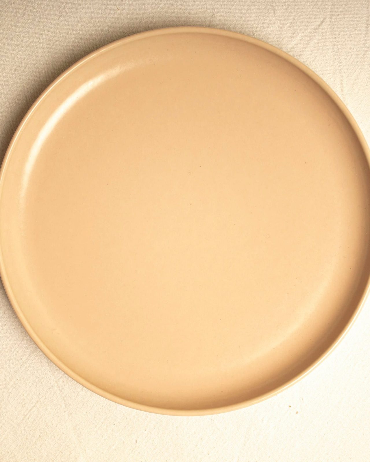 A butter-toned side plate photographed from above on a soft cream surface