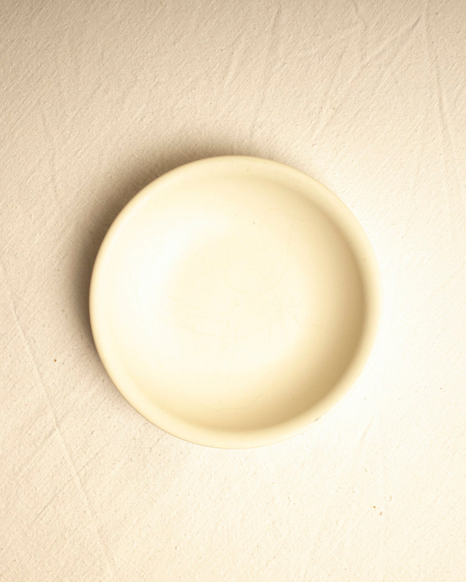 A deep cream bowl photographed from above on a warm ivory surface