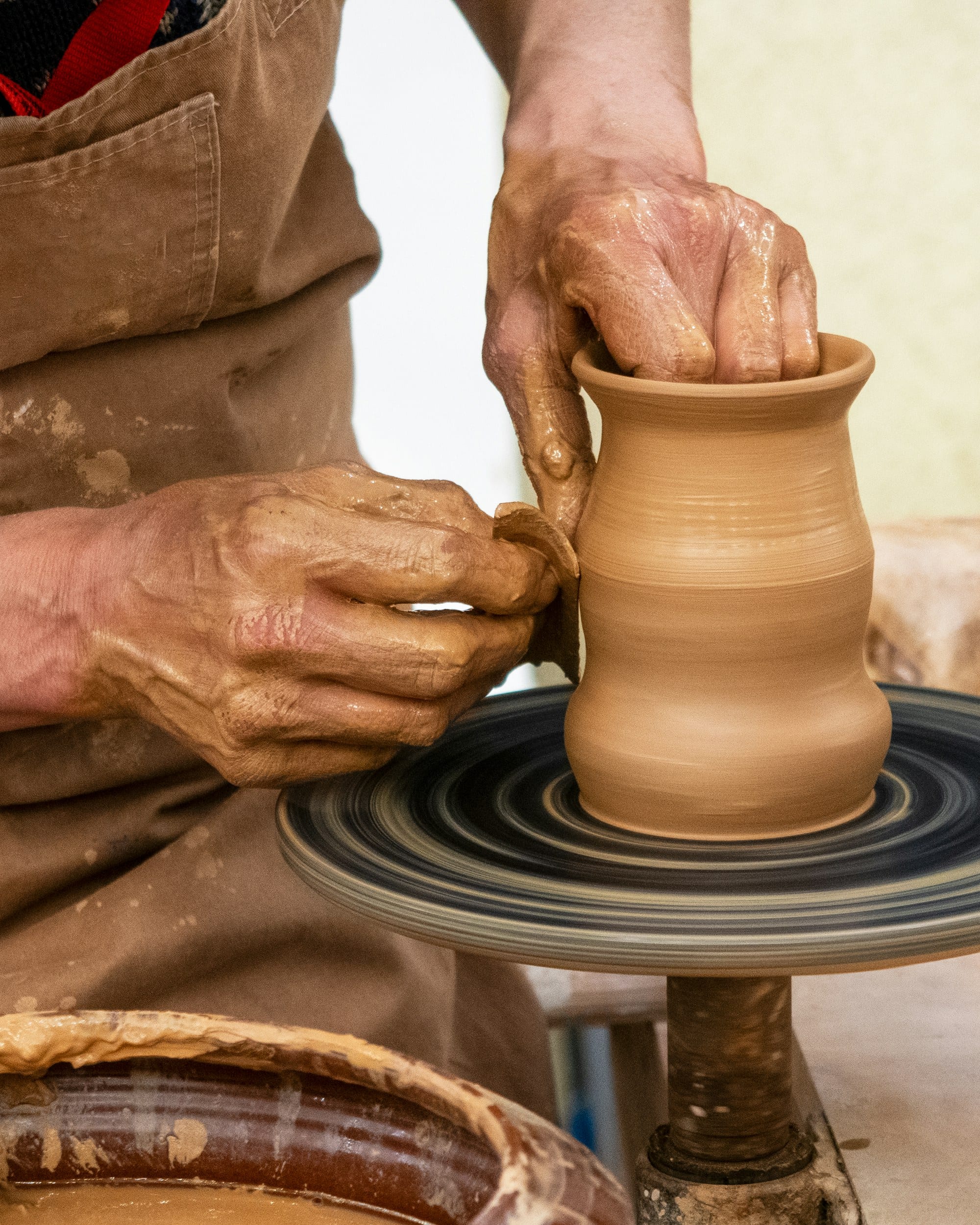 Two clay-covered hands centring a mound of stoneware on the wheel head