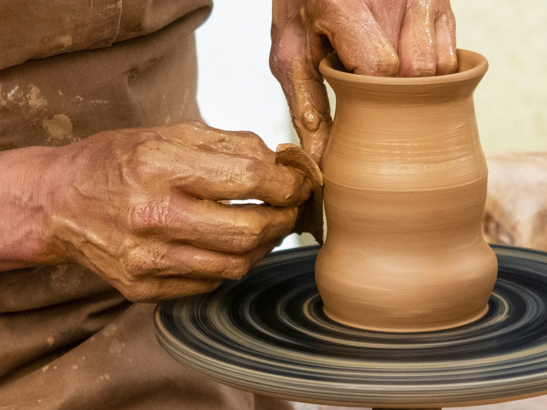 Two clay-covered hands centring a mound of stoneware on the wheel head