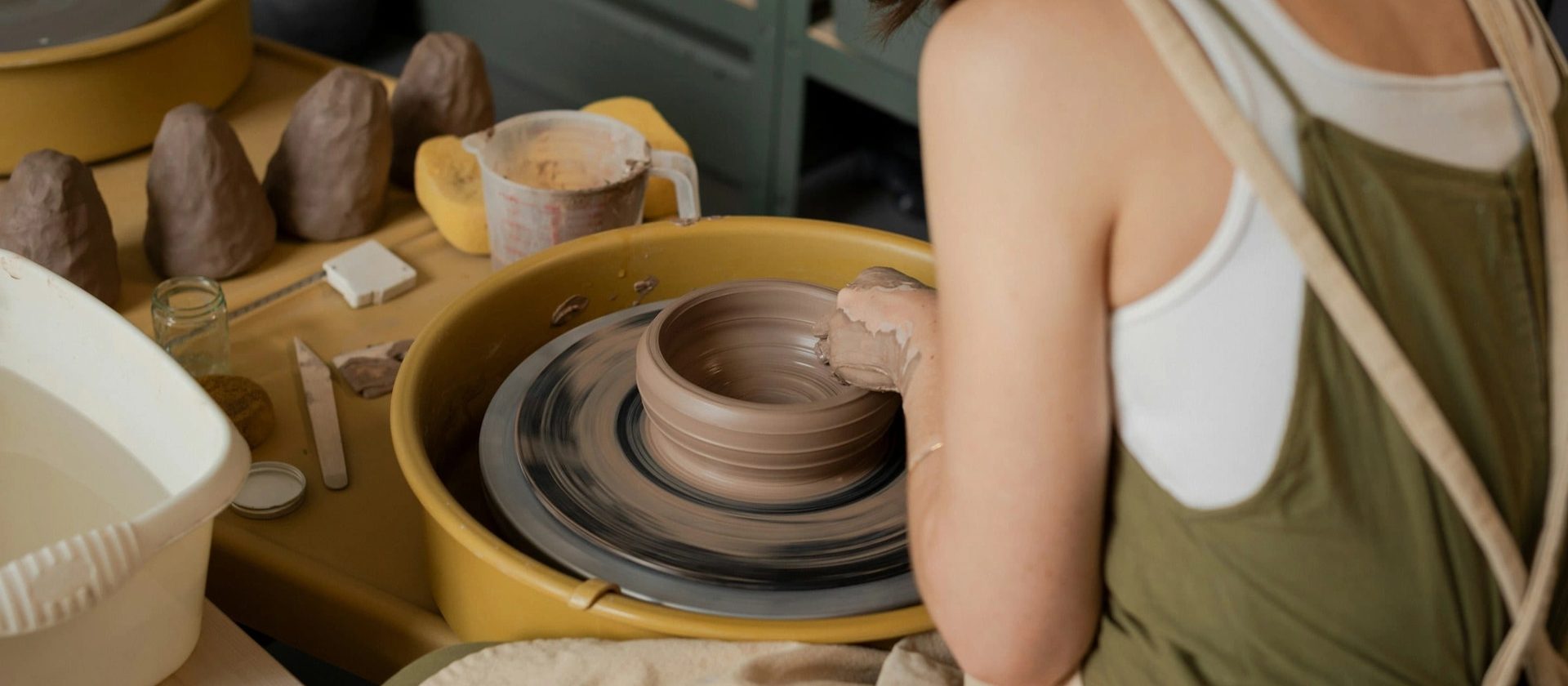 A ceramicist drawing the walls of a bowl upward on a spinning potter’s wheel