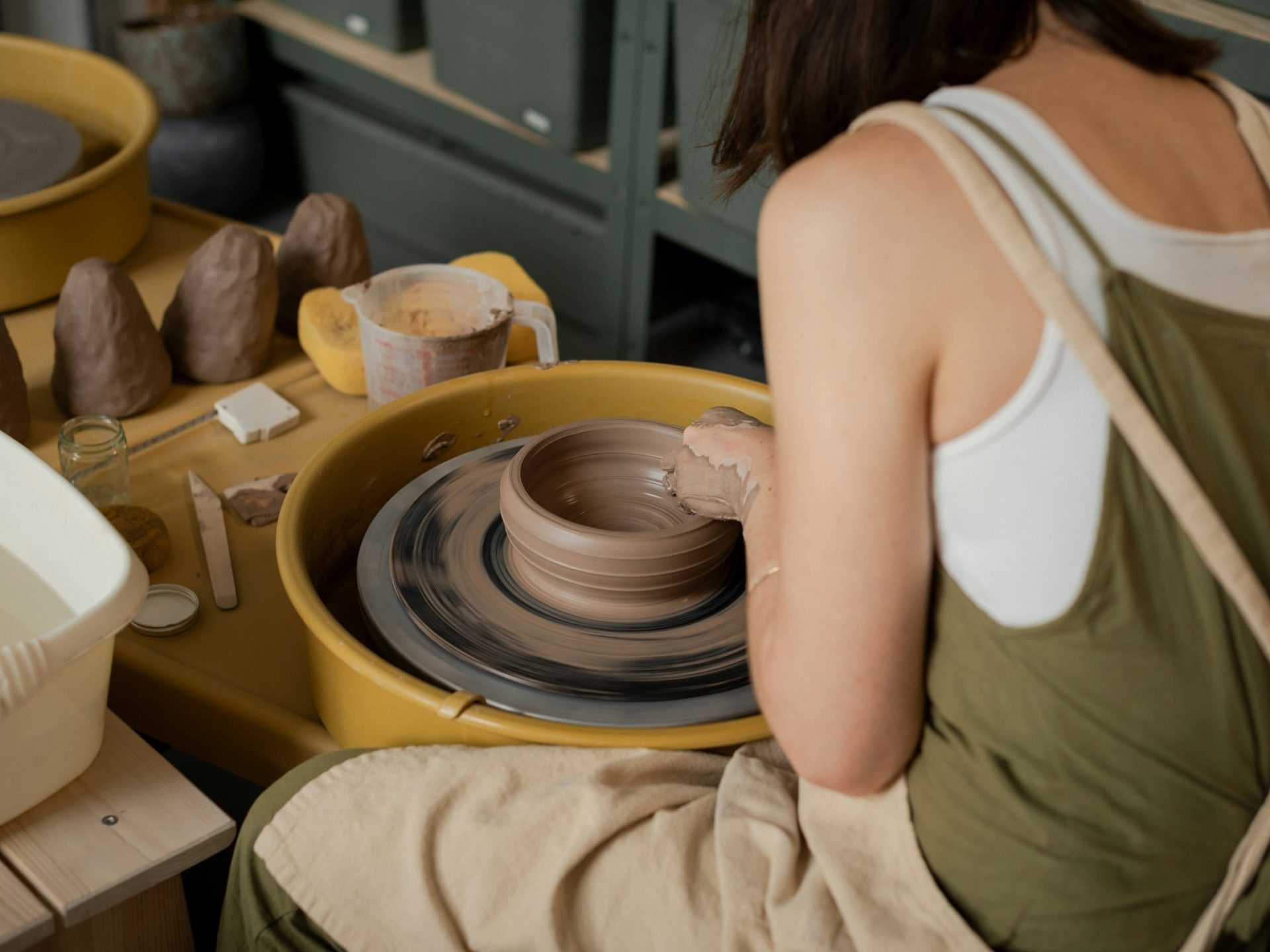 A ceramicist drawing the walls of a bowl upward on a spinning potter’s wheel
