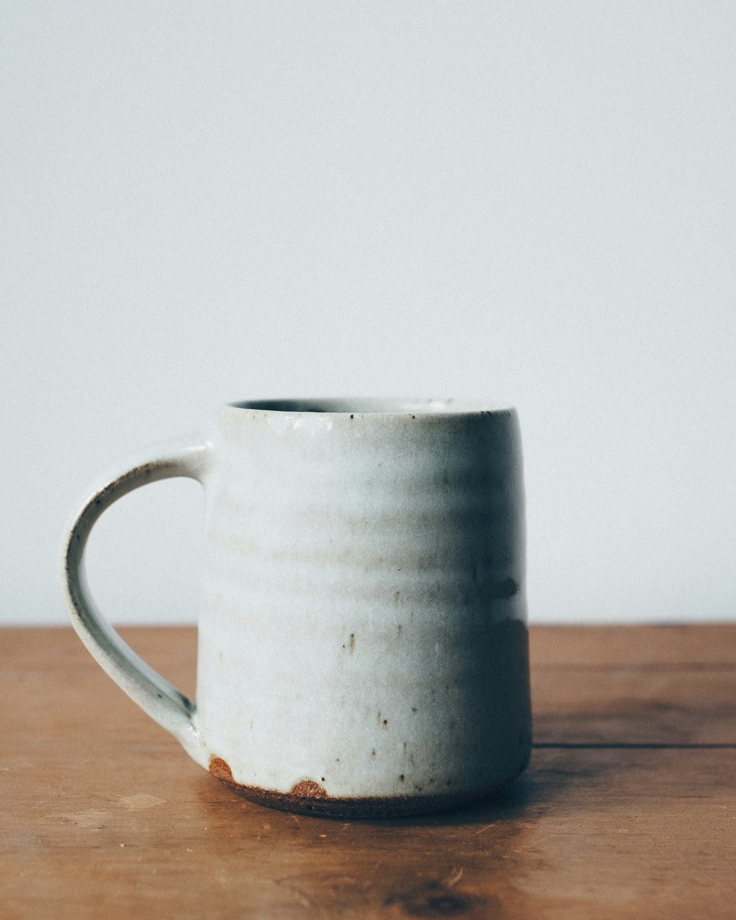 A white speckled mug resting on a worn oak table