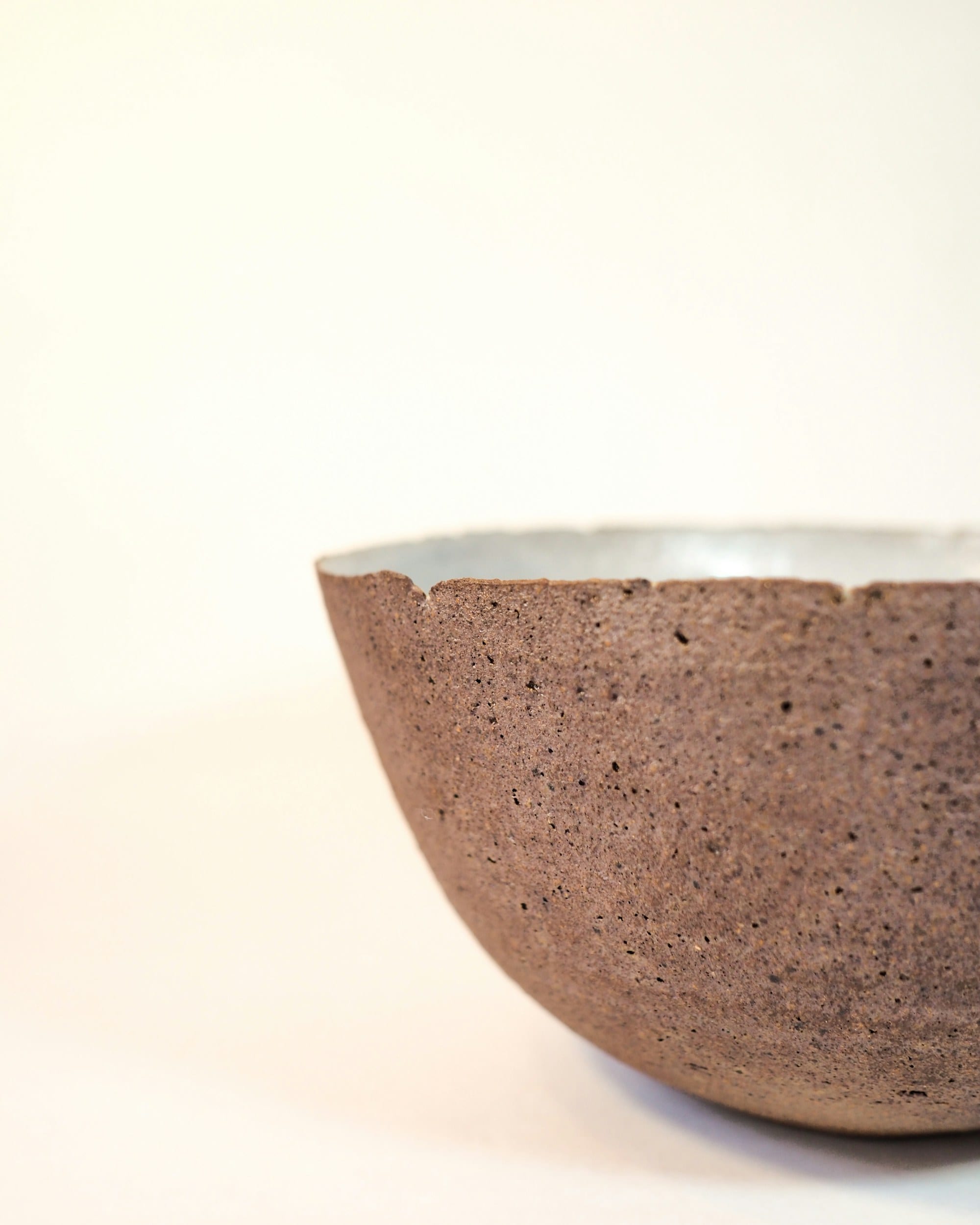 A coarse unglazed clay bowl with a smooth white glazed interior, lit against a pale ground