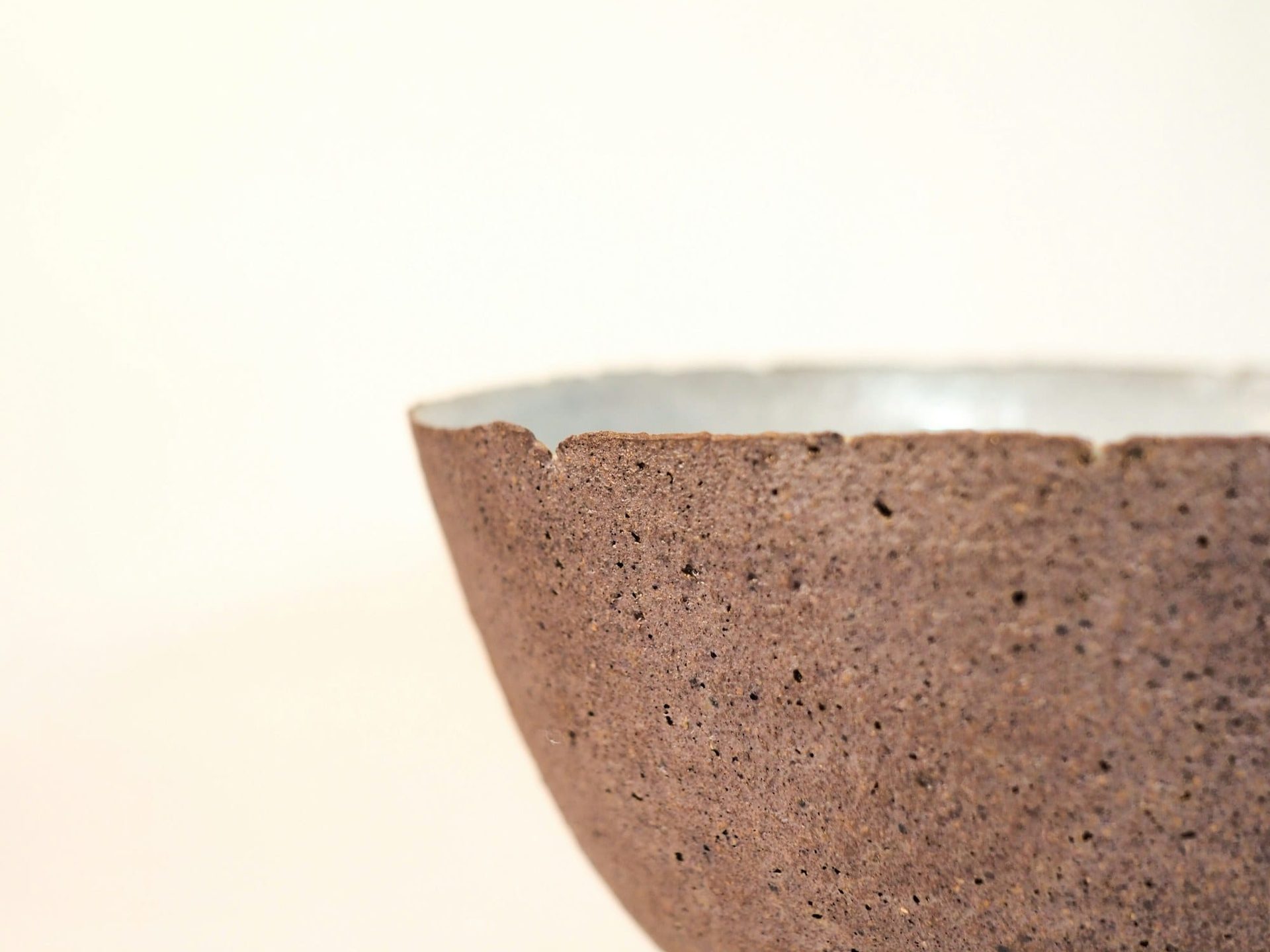 A coarse unglazed clay bowl with a smooth white glazed interior, lit against a pale ground